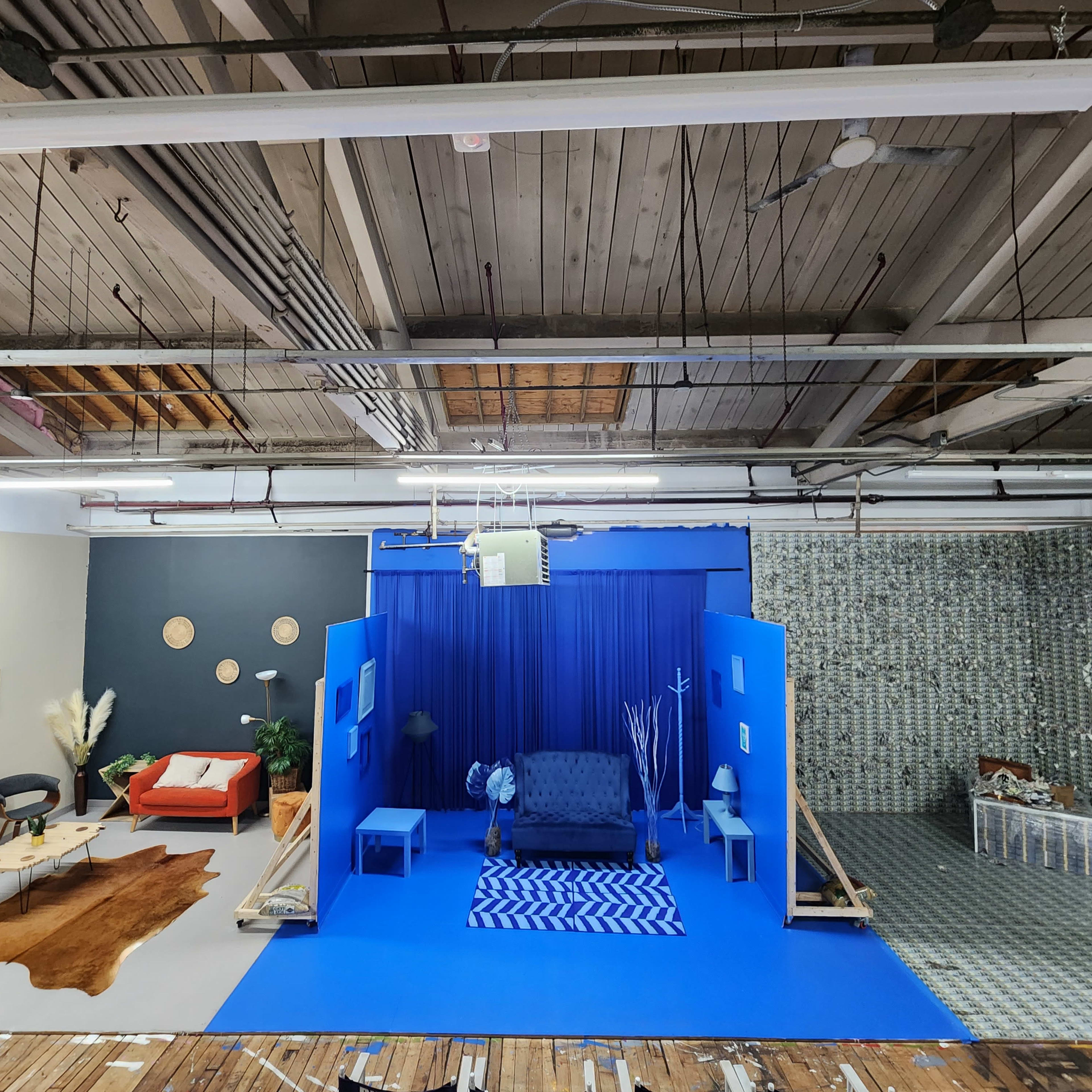 A large room divided into two distinct areas: one with a blue backdrop featuring a sofa and blue decor, and the other with neutral-colored furniture, artwork, and a textured wall.