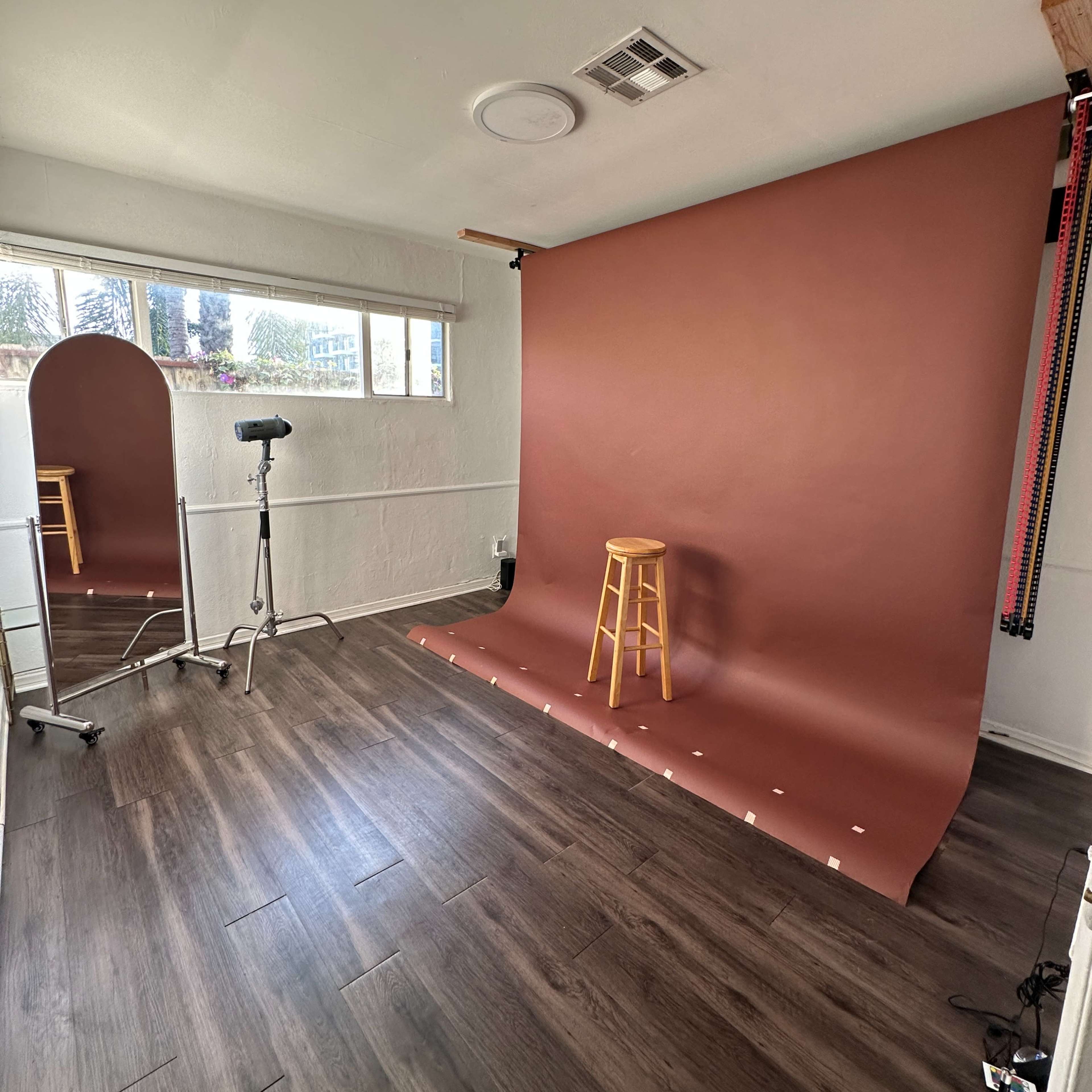 A photo studio setup featuring a brown backdrop, a wooden stool, and a camera on a tripod.