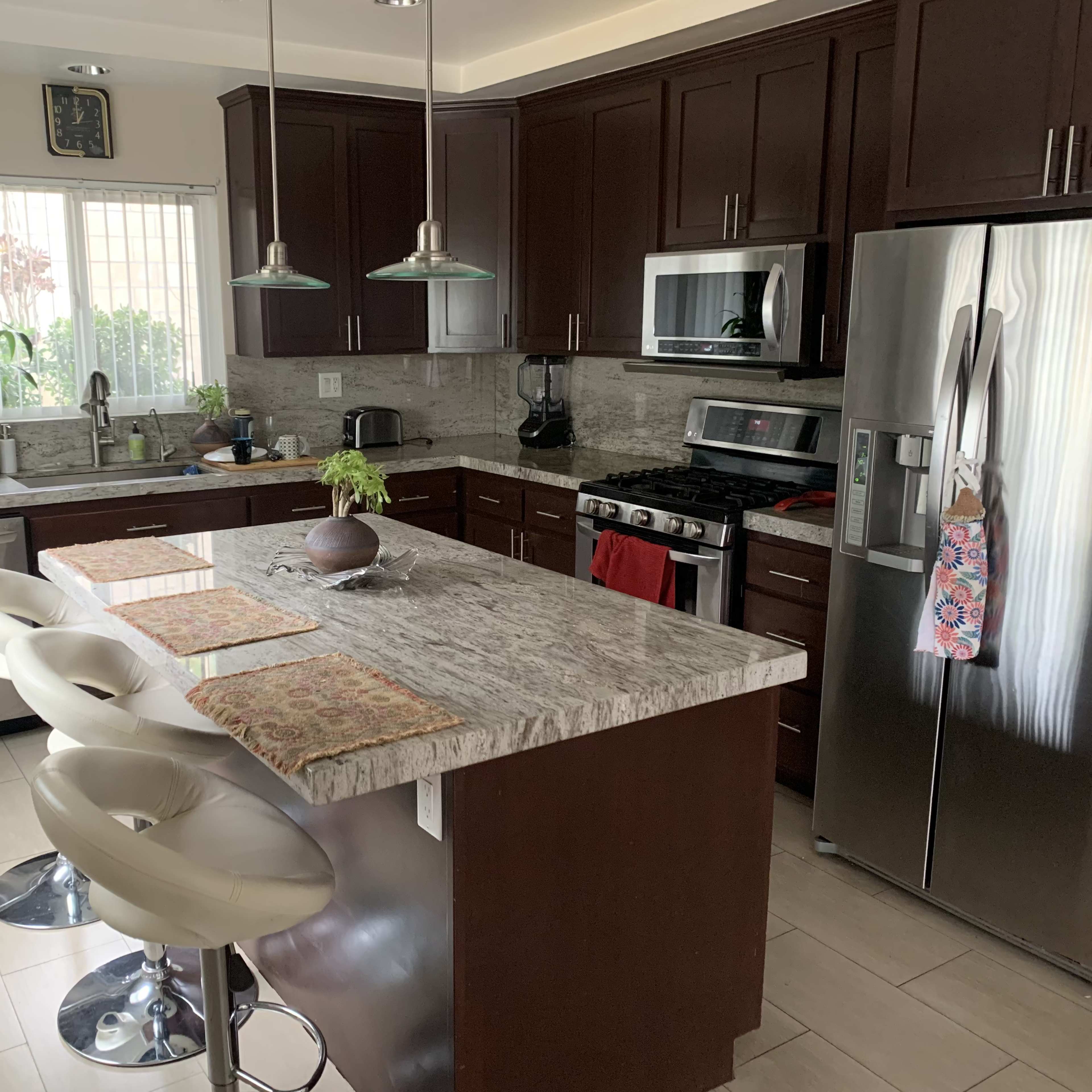 A modern kitchen with dark wooden cabinets, a granite countertop island with four white bar stools, and stainless steel appliances.