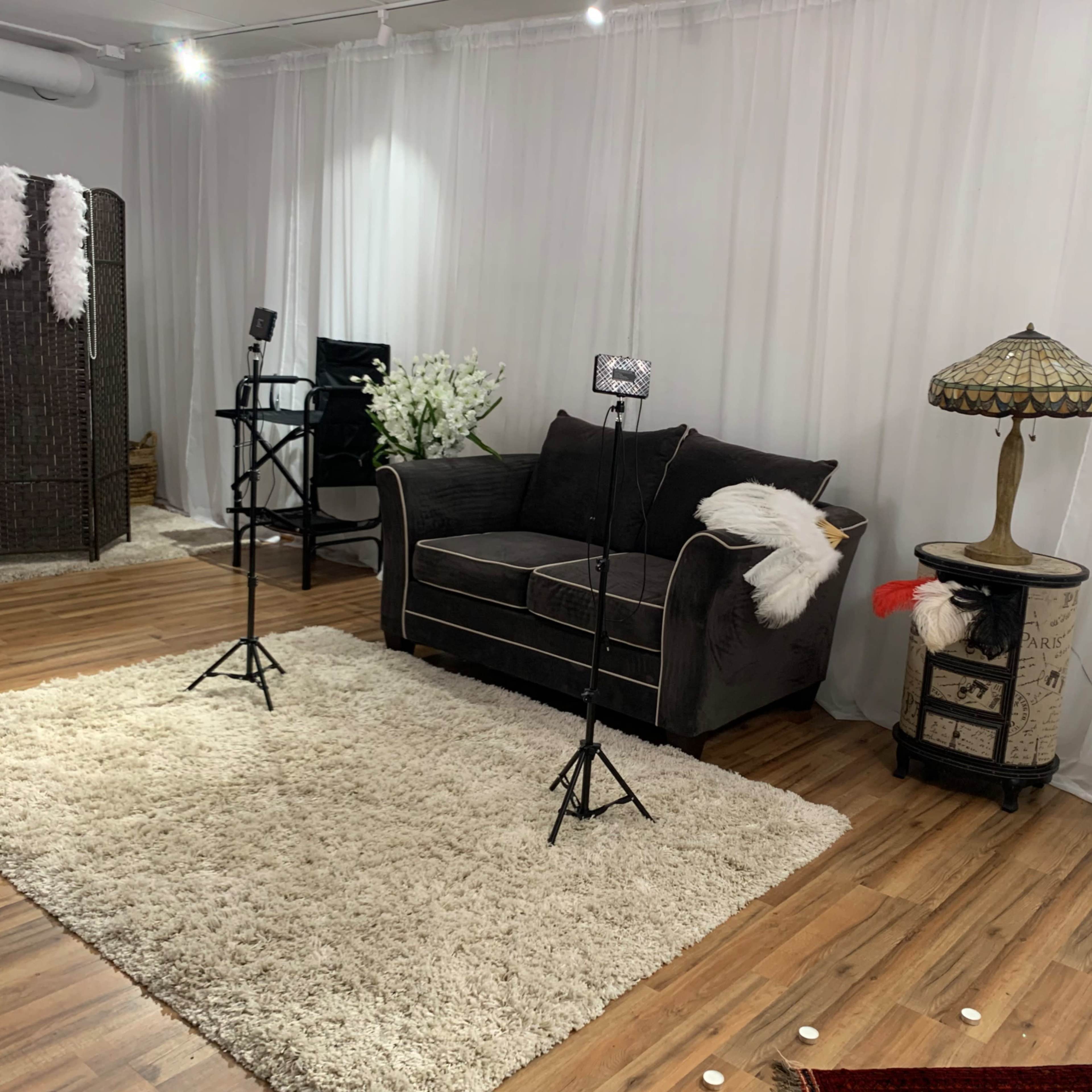 A cozy studio setup featuring a dark sofa, two lighting stands, a table lamp, and decorative elements on a plush rug.