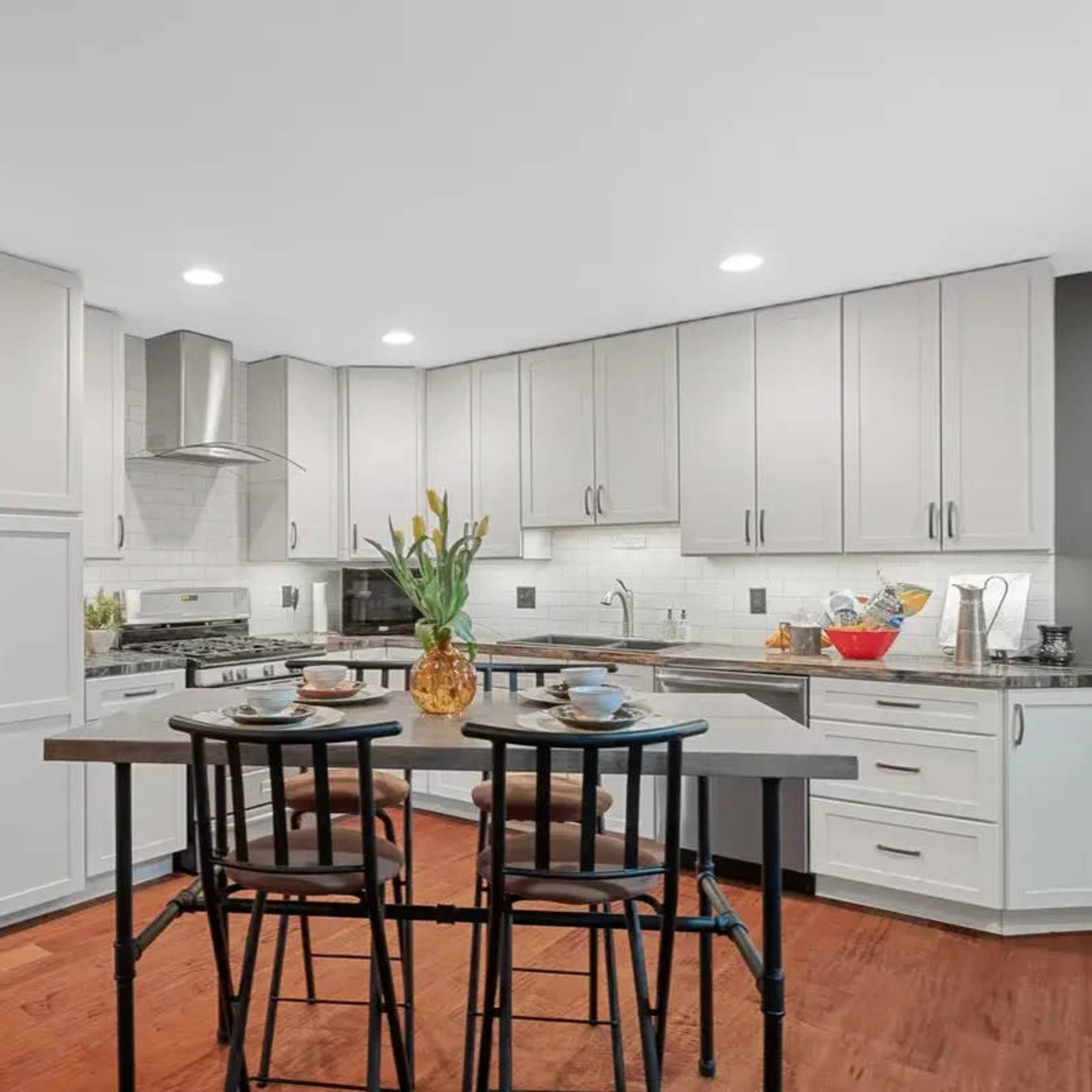 A modern kitchen features gray cabinets, stainless steel appliances, and a central table set for two.