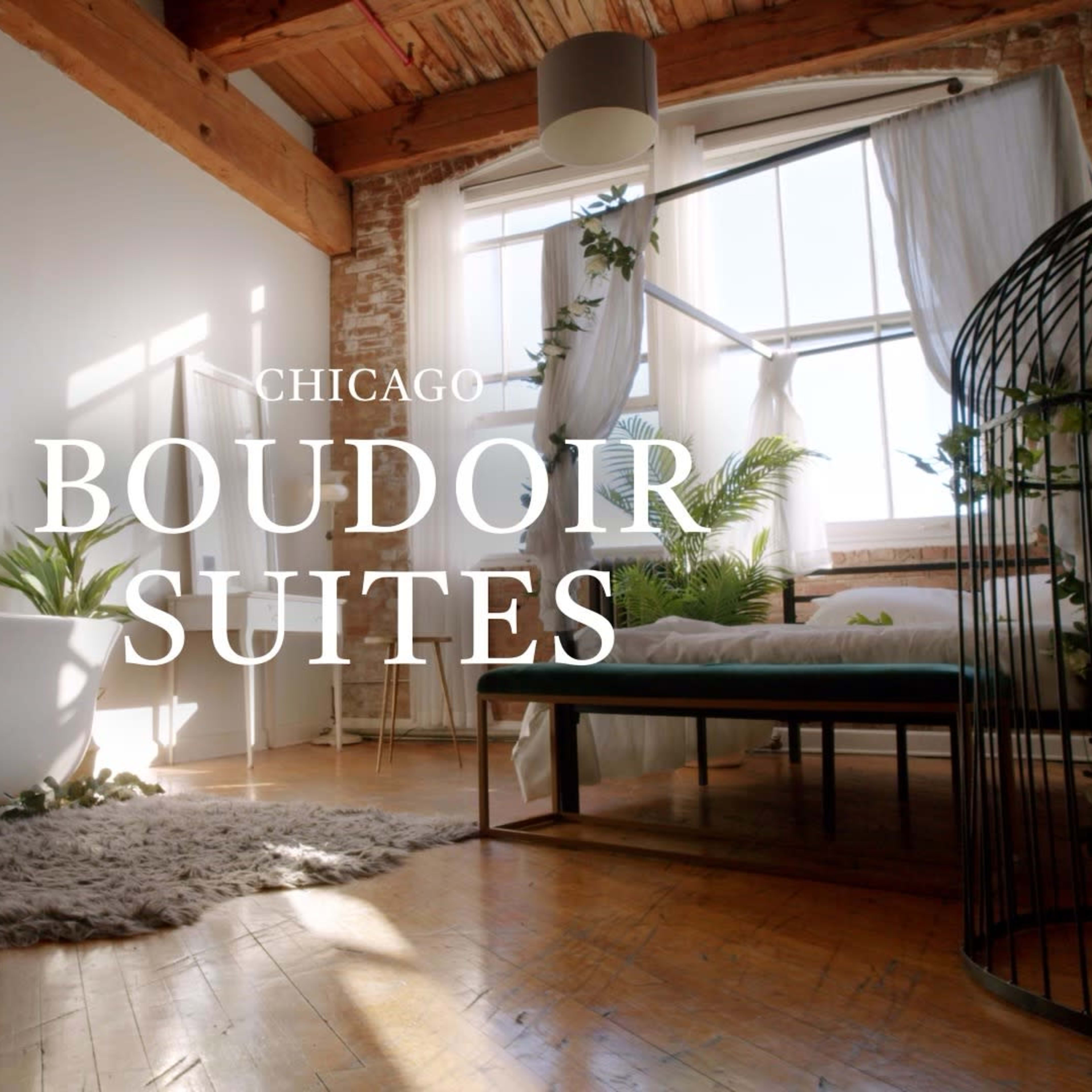 A bright, airy room with a freestanding bathtub, a bed, and greenery, featuring large windows and wooden beams.