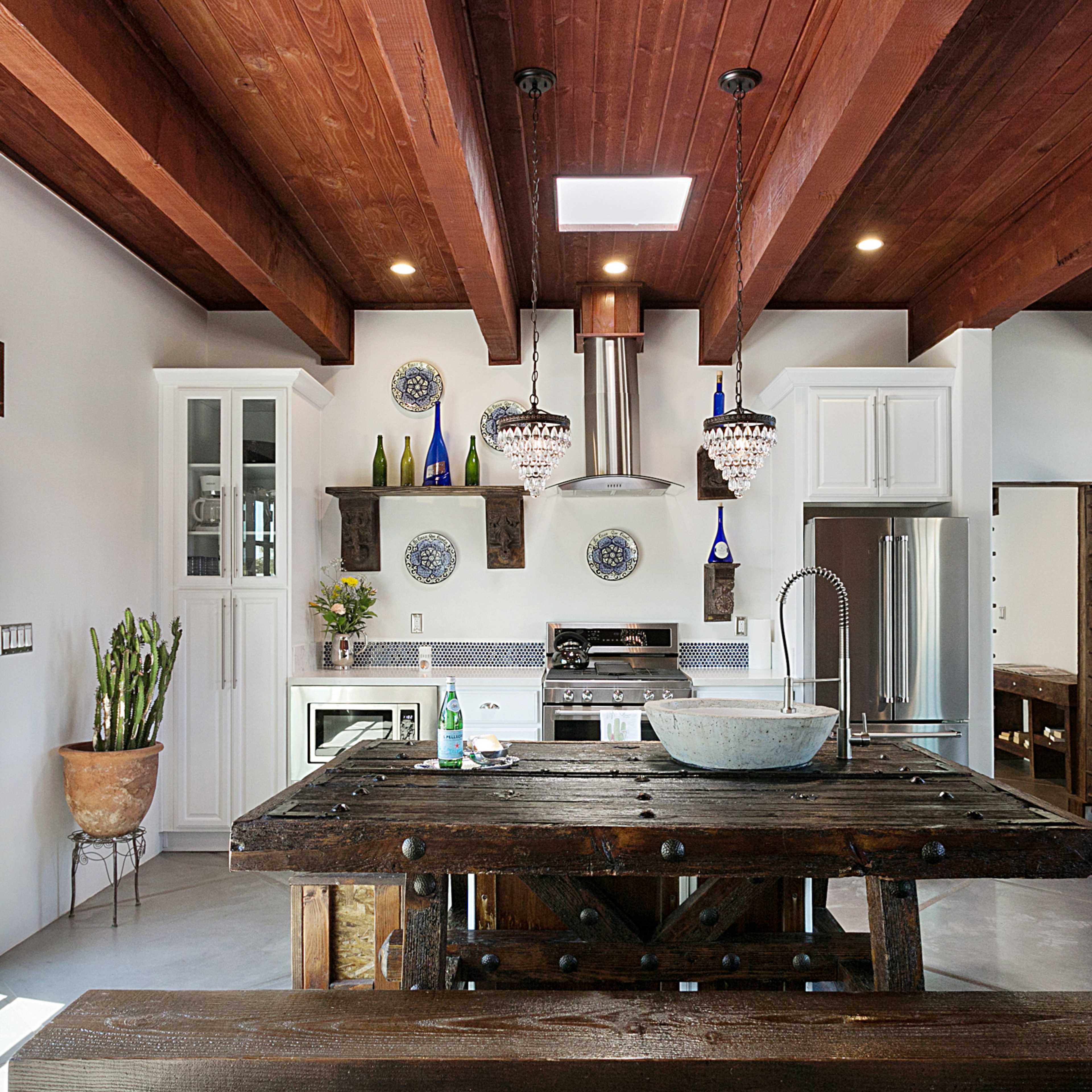 The kitchen features a large wooden table, stainless steel appliances, and exposed wooden beams on the ceiling.