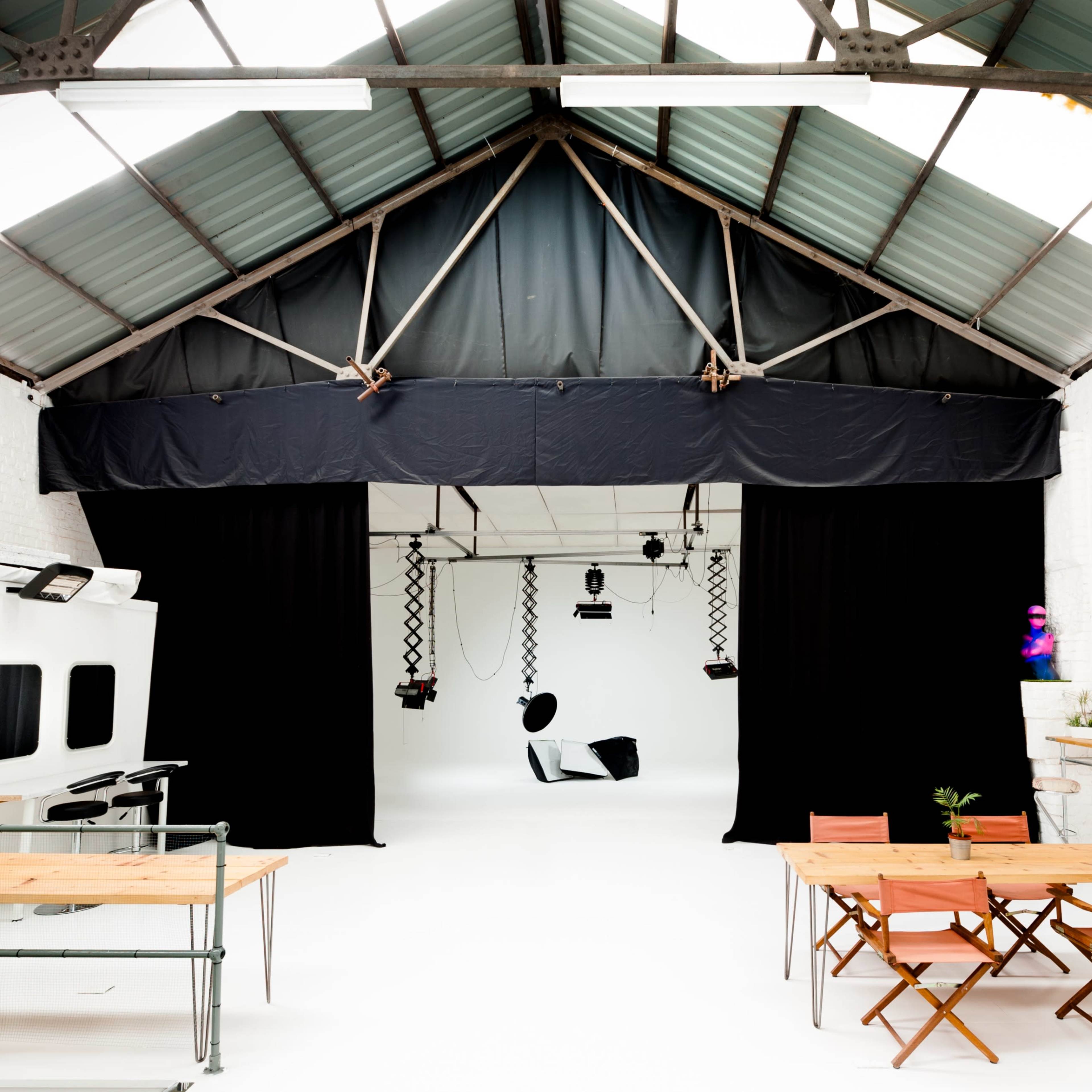 A spacious, minimalist studio with high ceilings, large black curtains, and wooden furniture arranged in two separate seating areas.