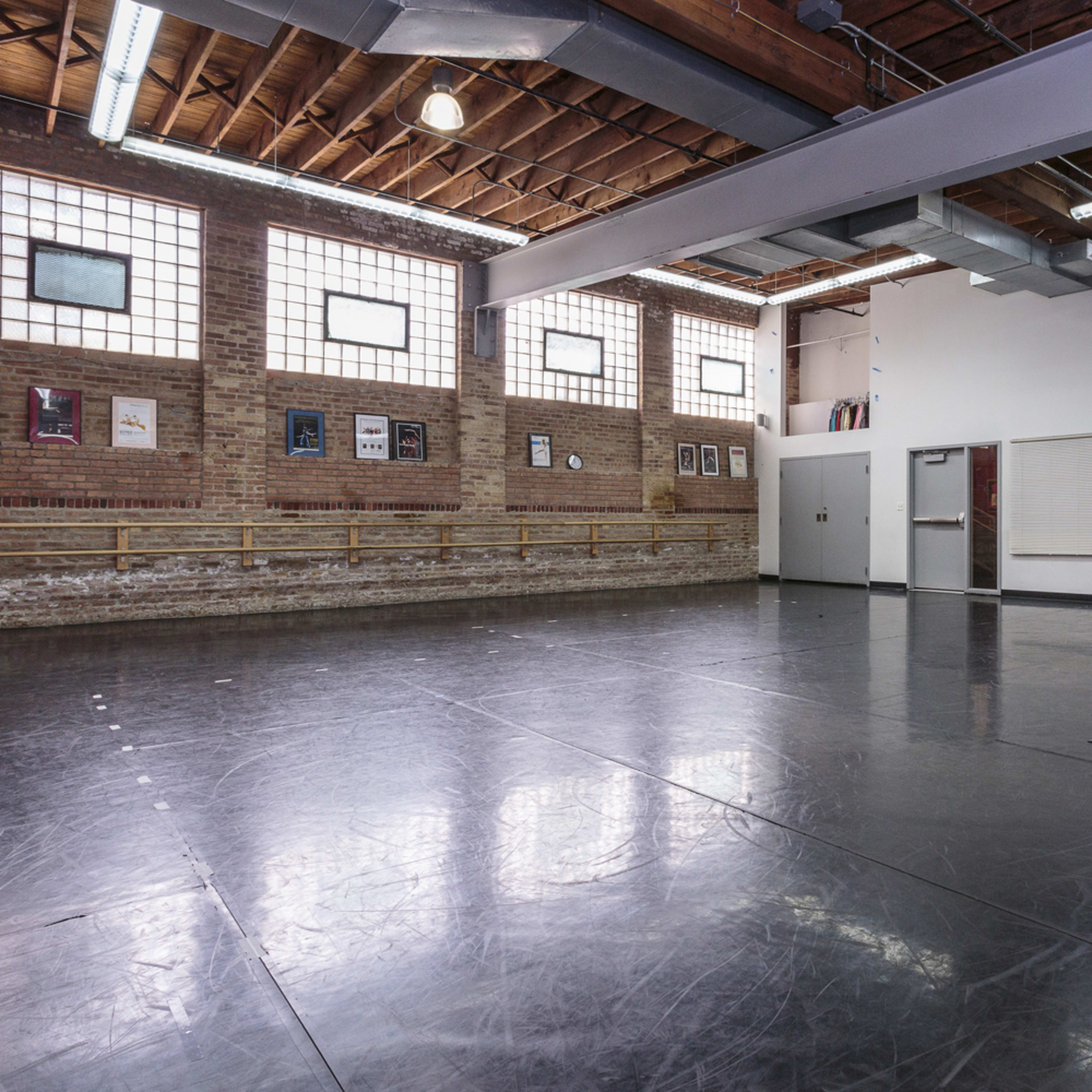A spacious dance studio with a polished black floor, large windows, and a mirrored wall.