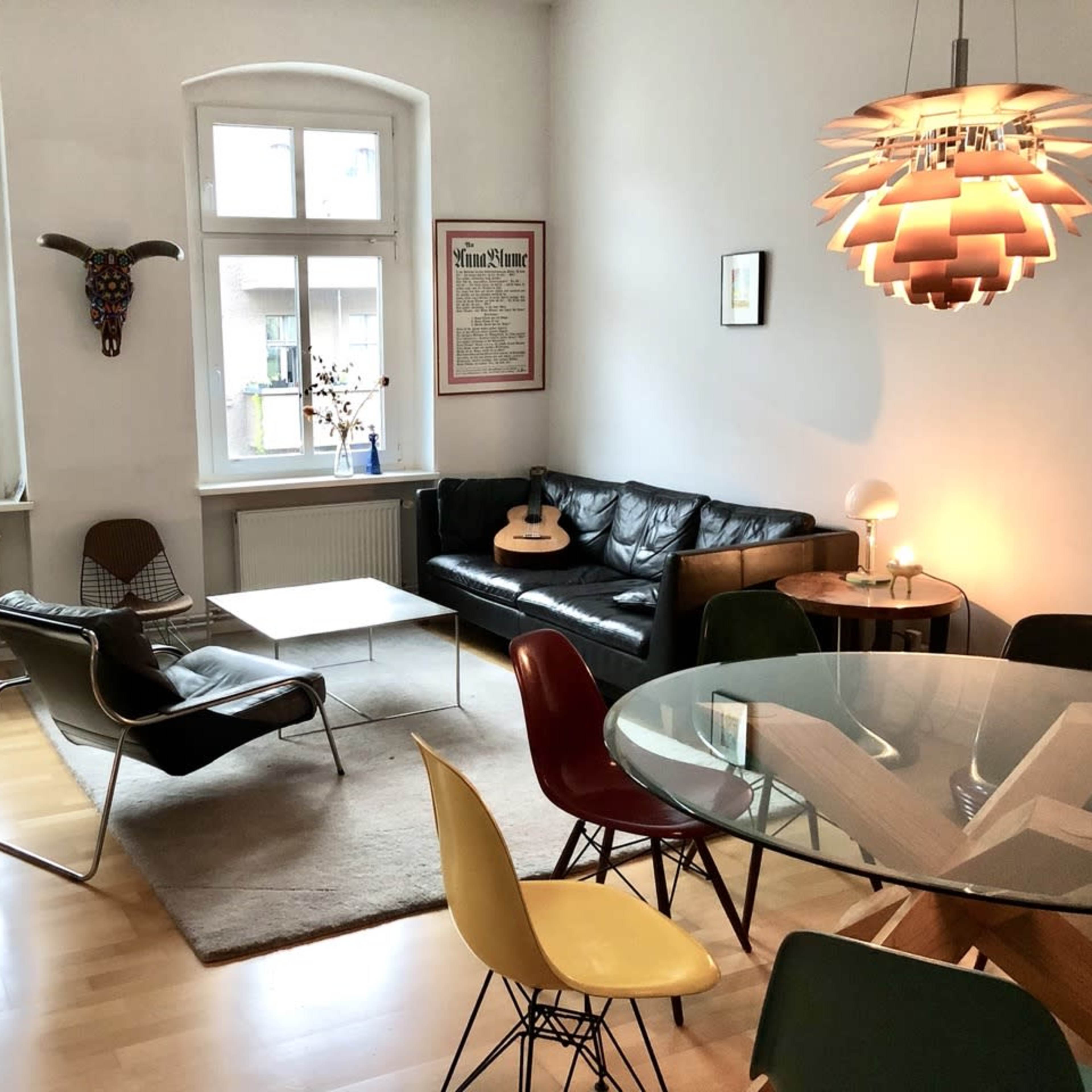 A modern living area featuring a black leather sofa, a glass dining table with colorful chairs, and an acoustic guitar on a coffee table.