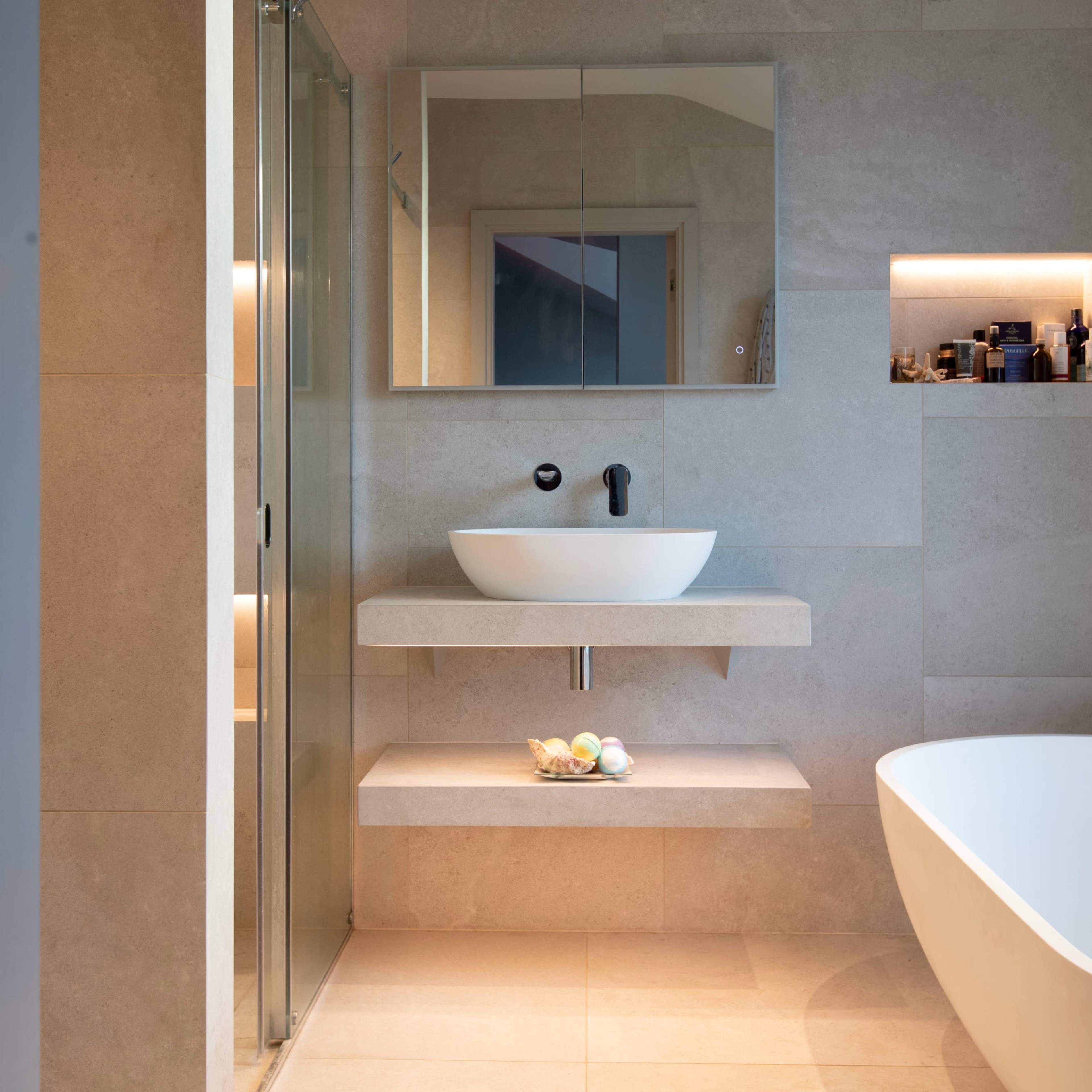 A modern bathroom featuring a wall-mounted sink above a stone shelf, a glass shower enclosure, a freestanding bathtub, and recessed lighting.