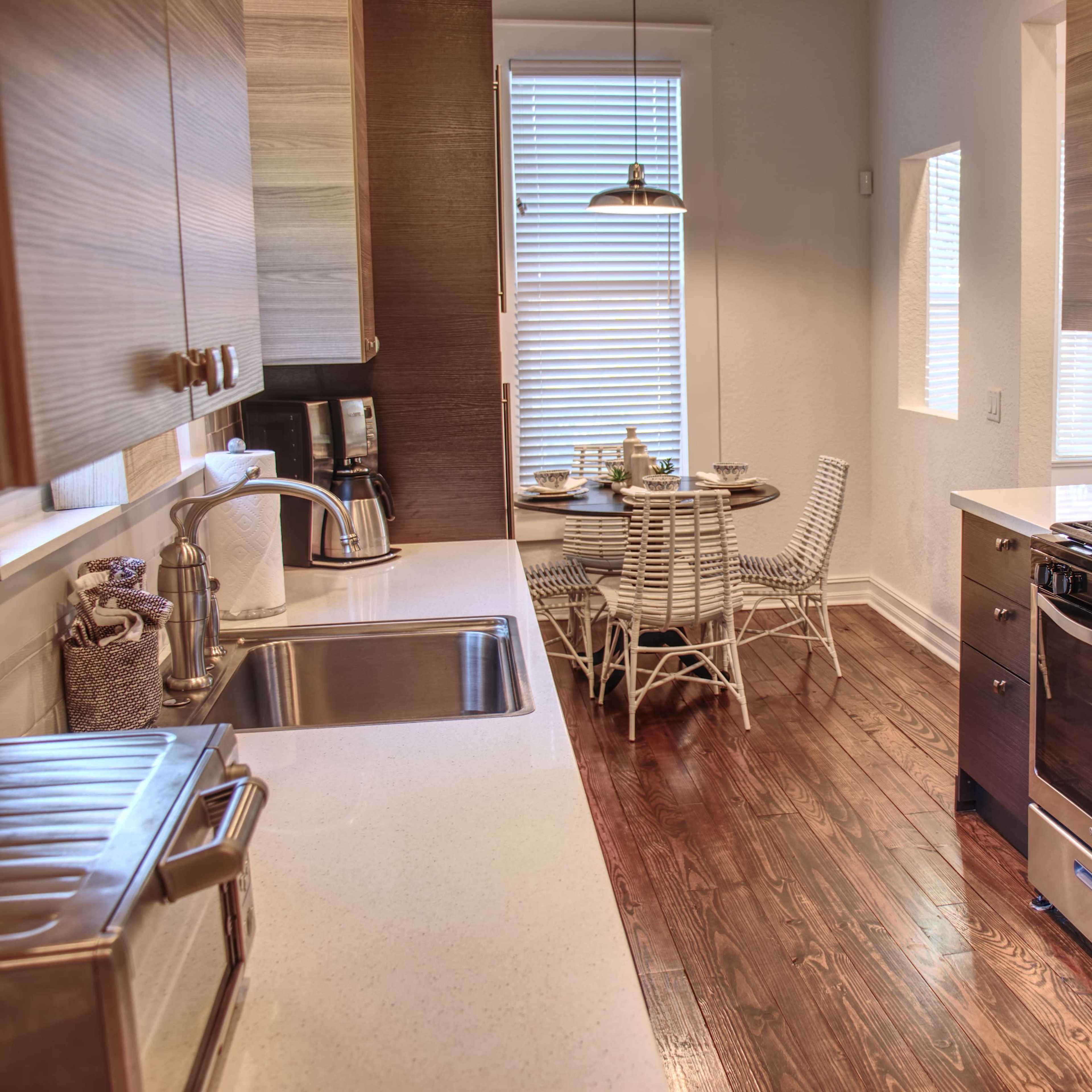 A modern kitchen with stainless steel appliances, wooden cabinetry, and a small dining area featuring a round table and chairs.