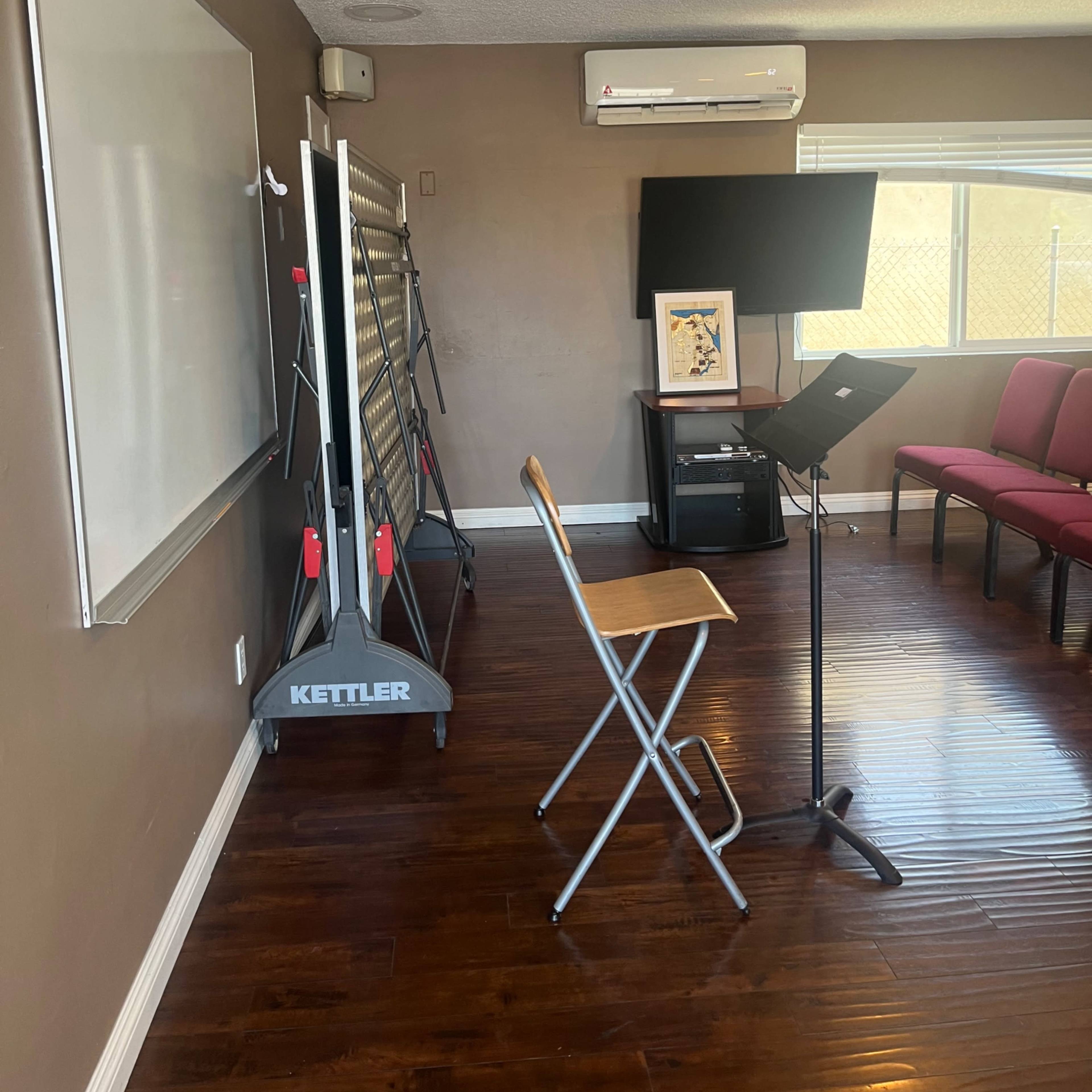 A meeting room featuring a whiteboard, a folding screen on wheels, a music stand, a wooden chair, and red upholstered chairs along the wall.