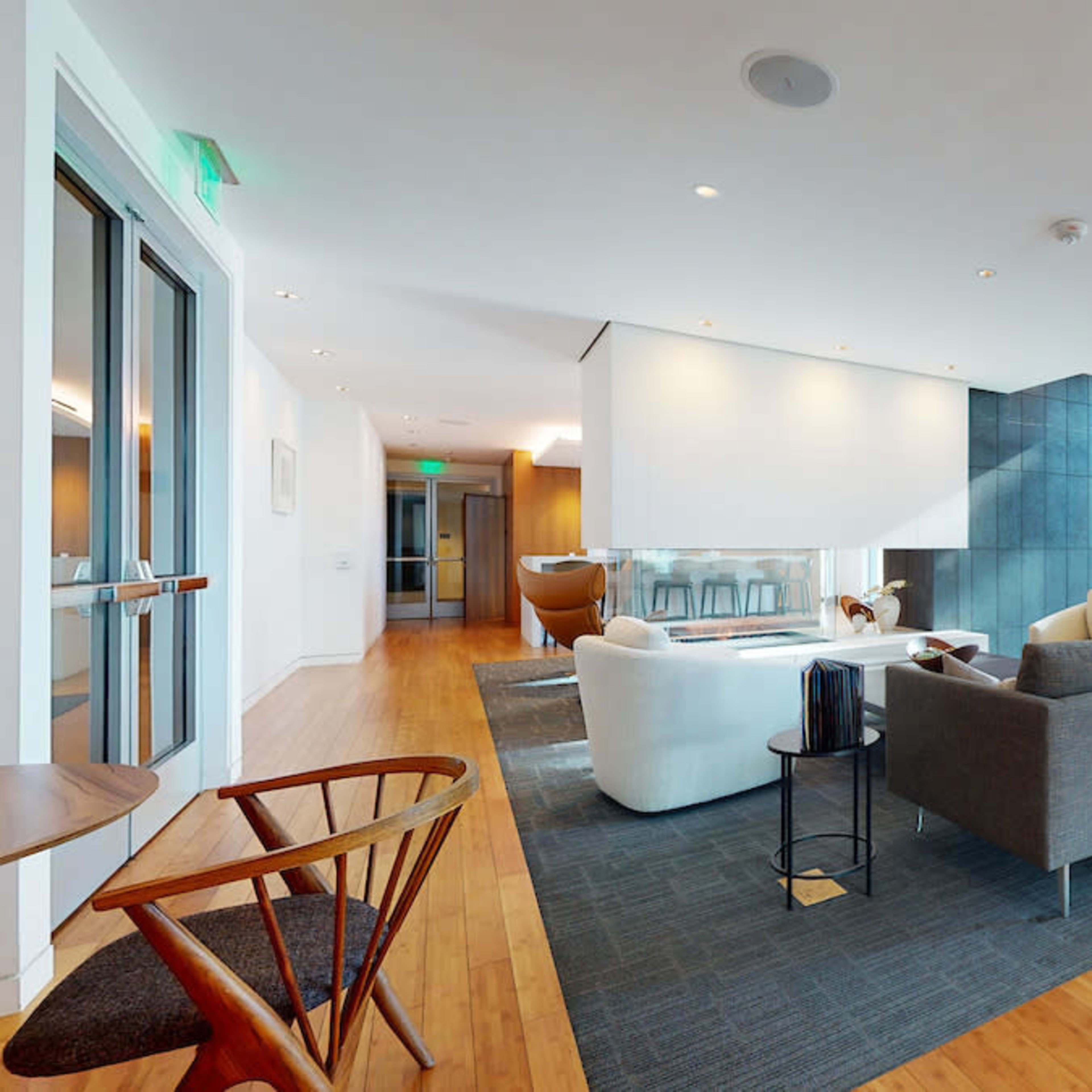 A modern lounge area with large windows, comfortable seating, and hardwood flooring.