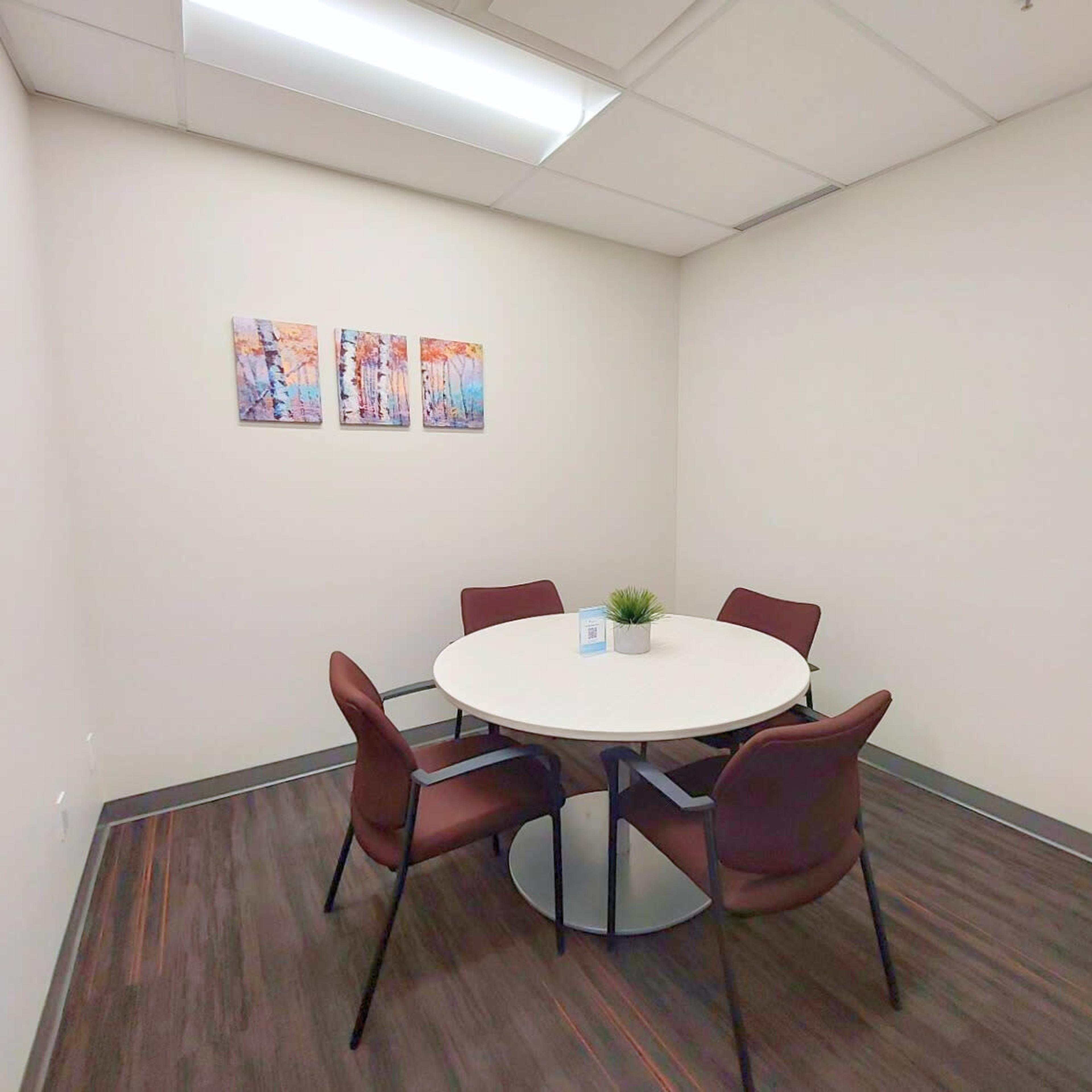 A small meeting room features a round table with four chairs and colorful artwork on the wall.