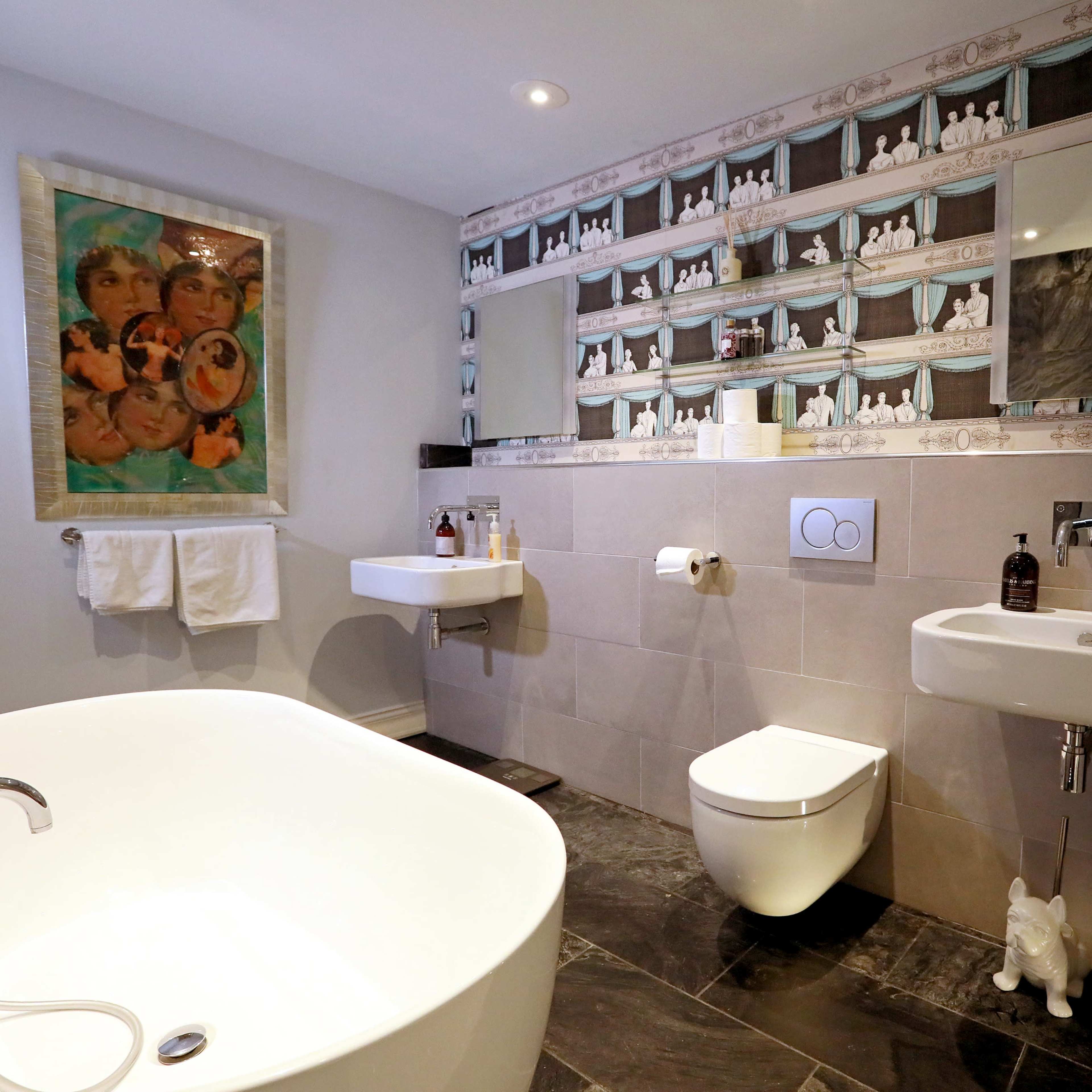 A modern bathroom featuring a freestanding bathtub, a wall with decorative tiles, and a double mirror above a wall-mounted sink.