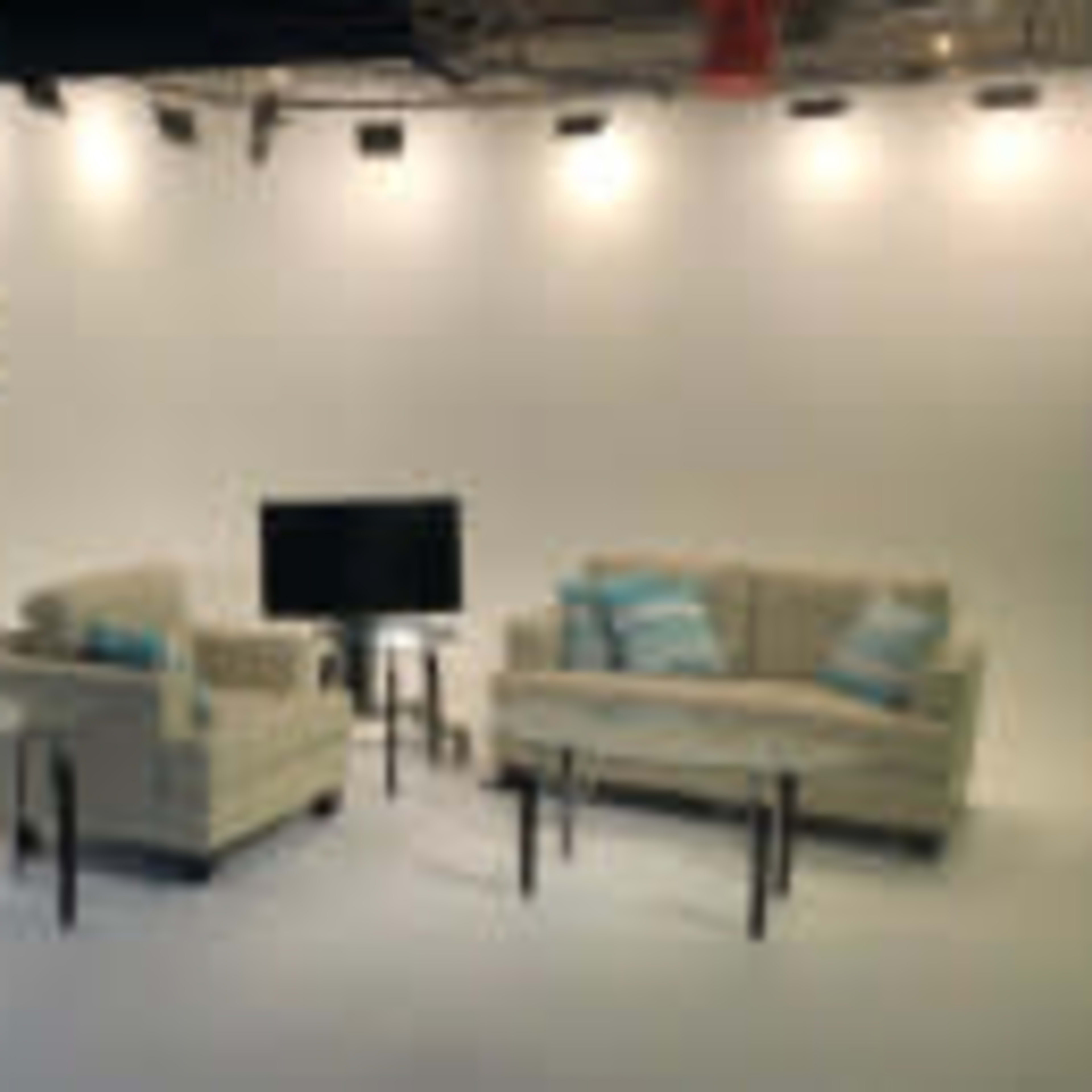 A two-sofa set with light cushions and a glass coffee table is arranged in a well-lit studio space.