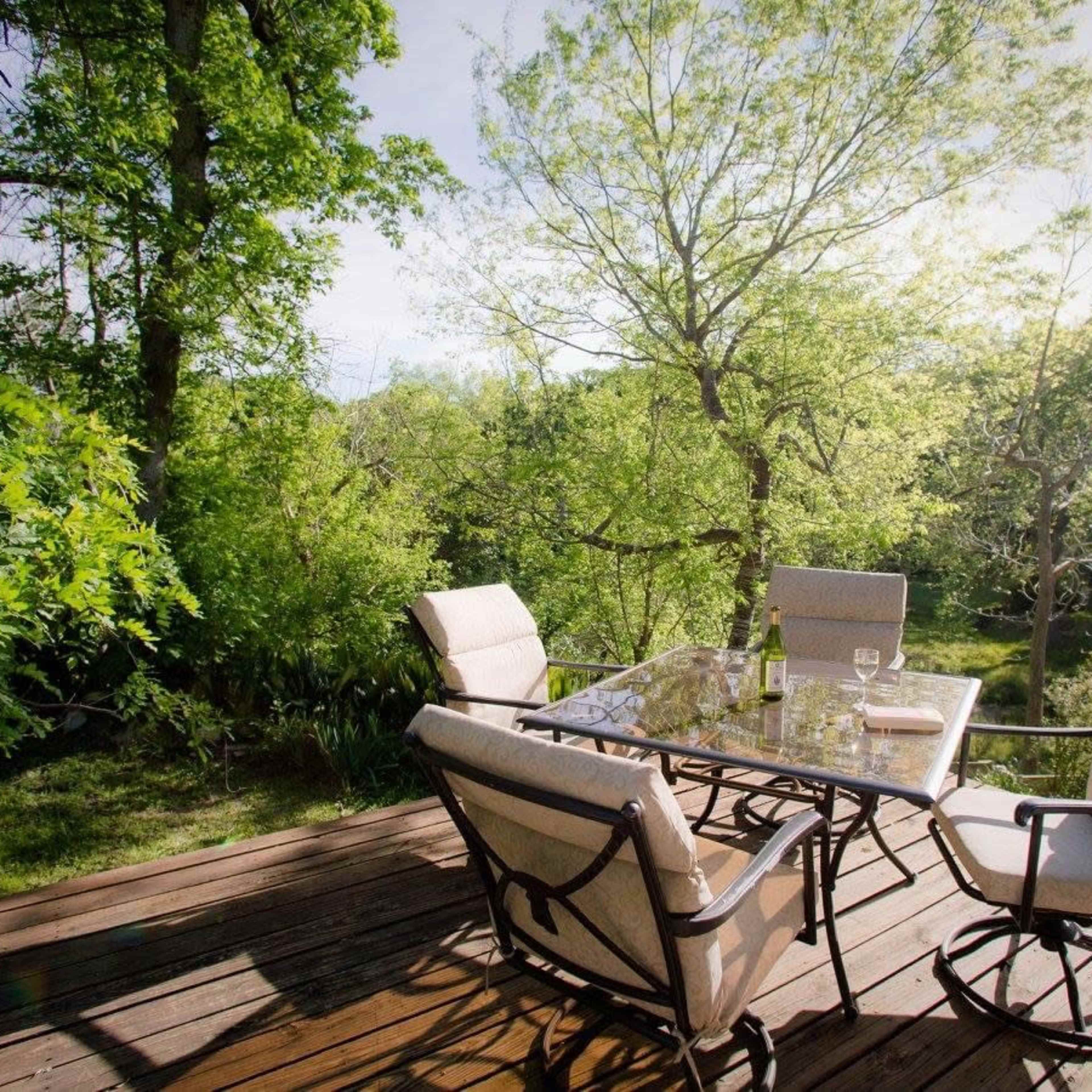 A patio area features a glass table surrounded by four cushioned chairs, set amidst a lush green garden.