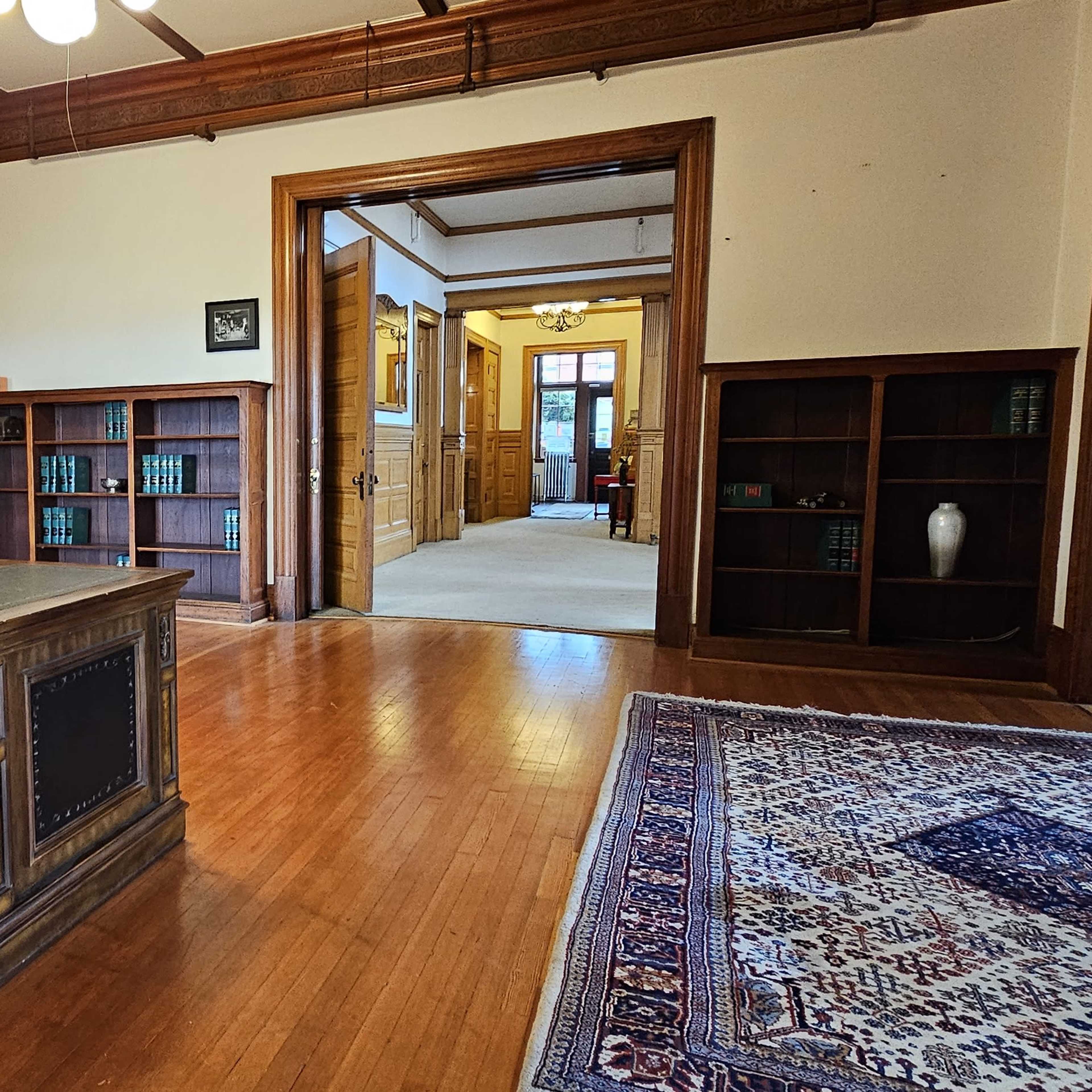 A wooden desk with a lamp in a spacious office featuring bookshelves and a doorway leading to another room.