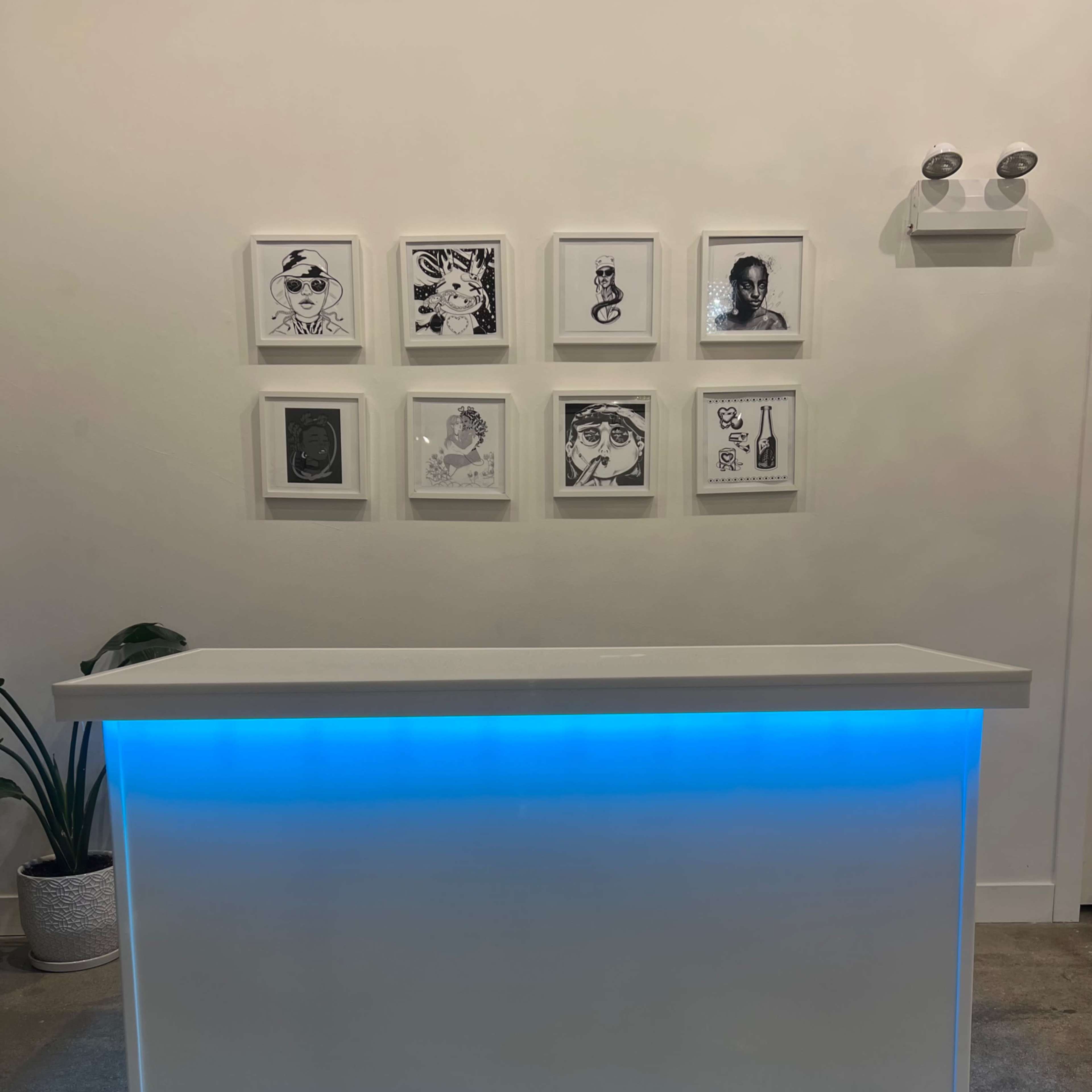 A modern reception desk with a blue-lit base is positioned in front of a wall displaying framed black-and-white artworks.