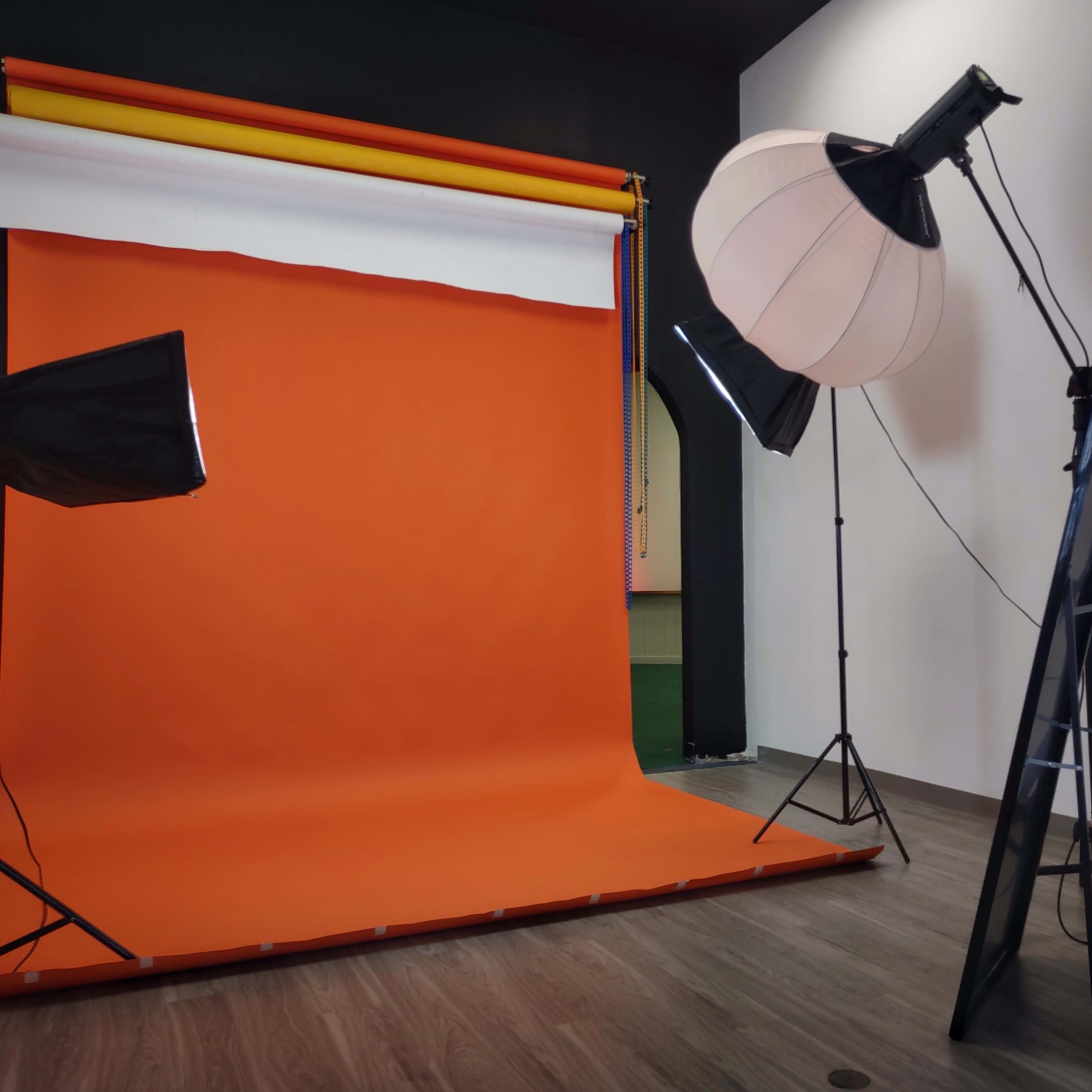 A photography studio with an orange backdrop, lighting equipment, and a large softbox set up for a photoshoot.