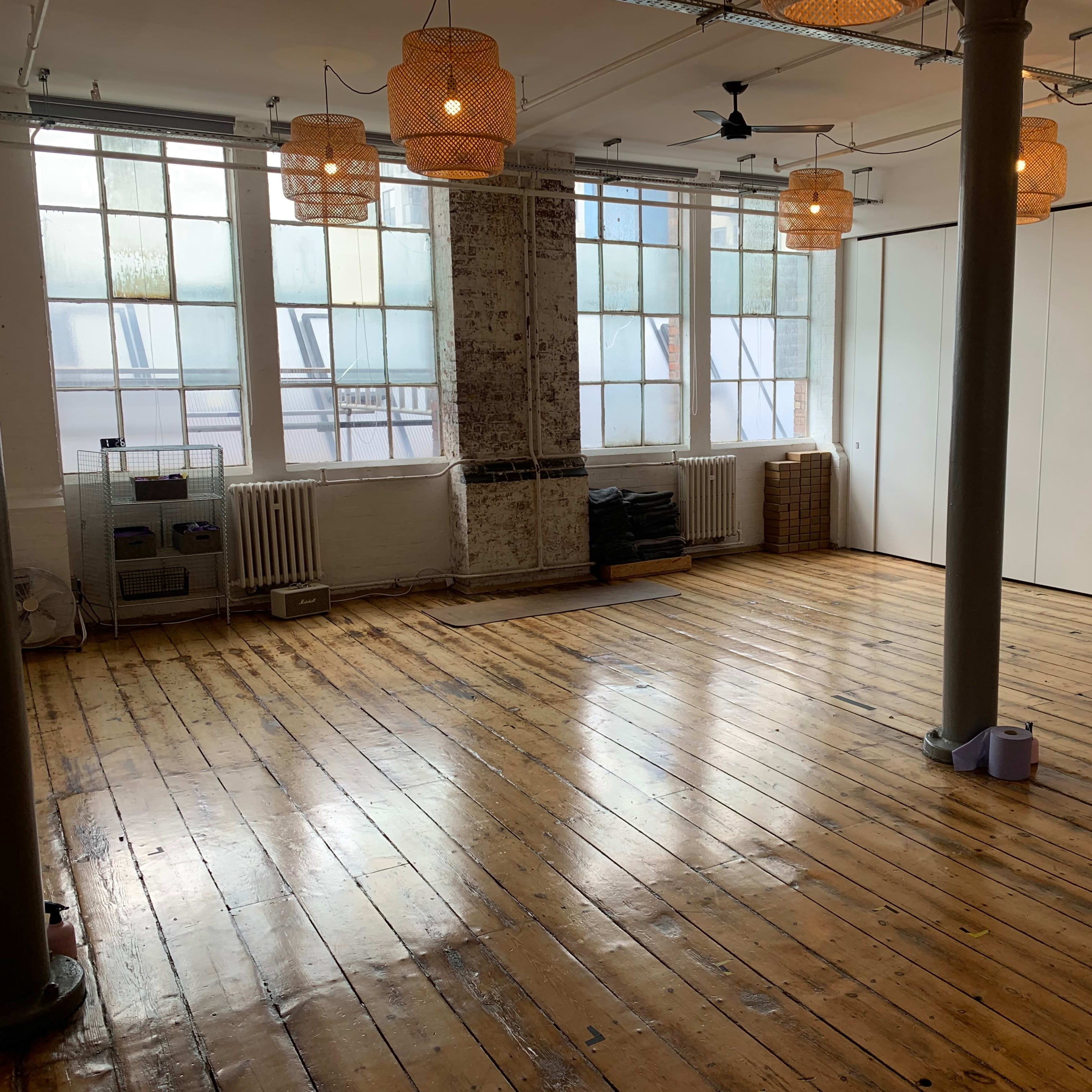 An empty room with wooden floors, large windows allowing natural light, and ceiling lamps made of woven material.