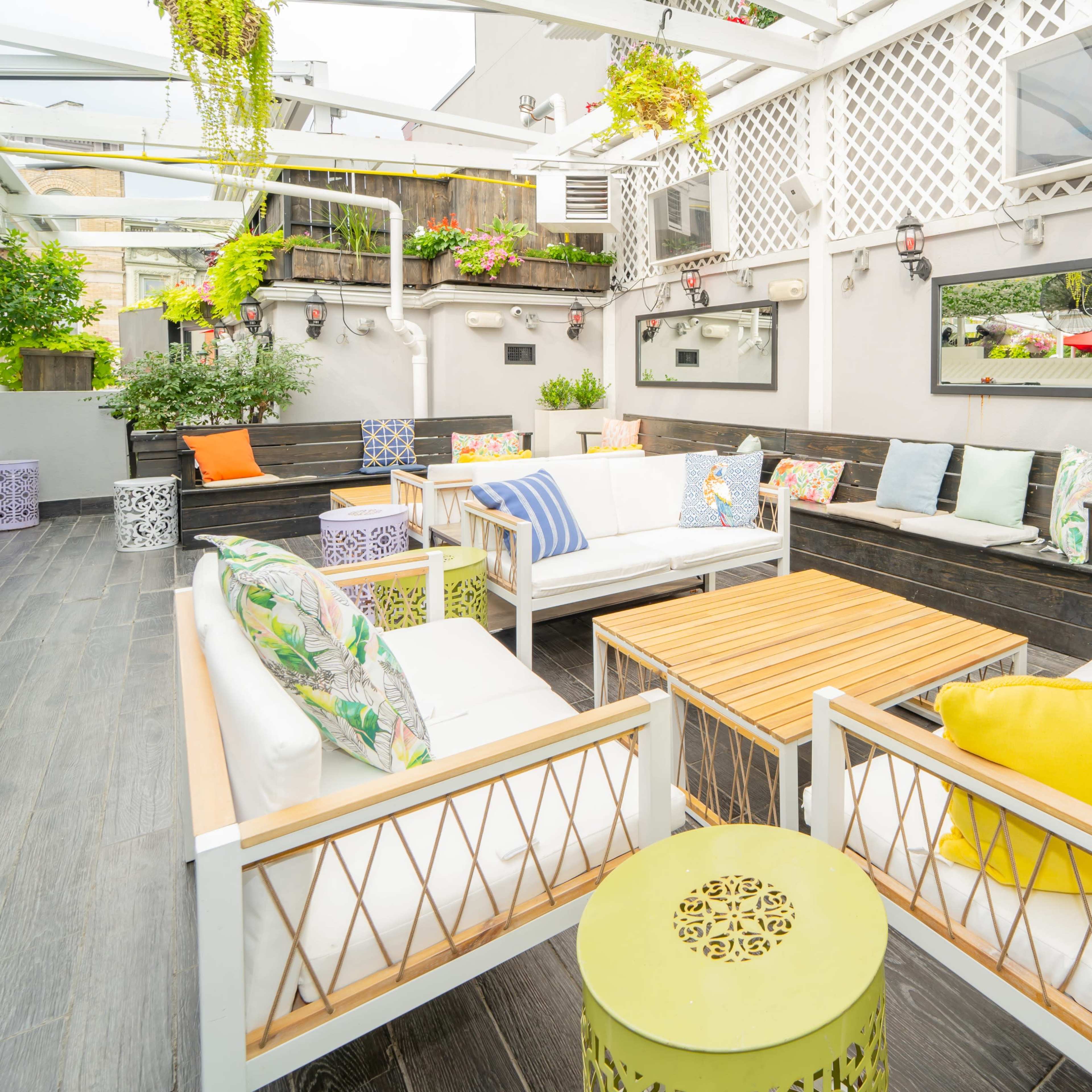 A modern outdoor seating area with white couches, wooden tables, and decorative plants arranged around a stylish patio.