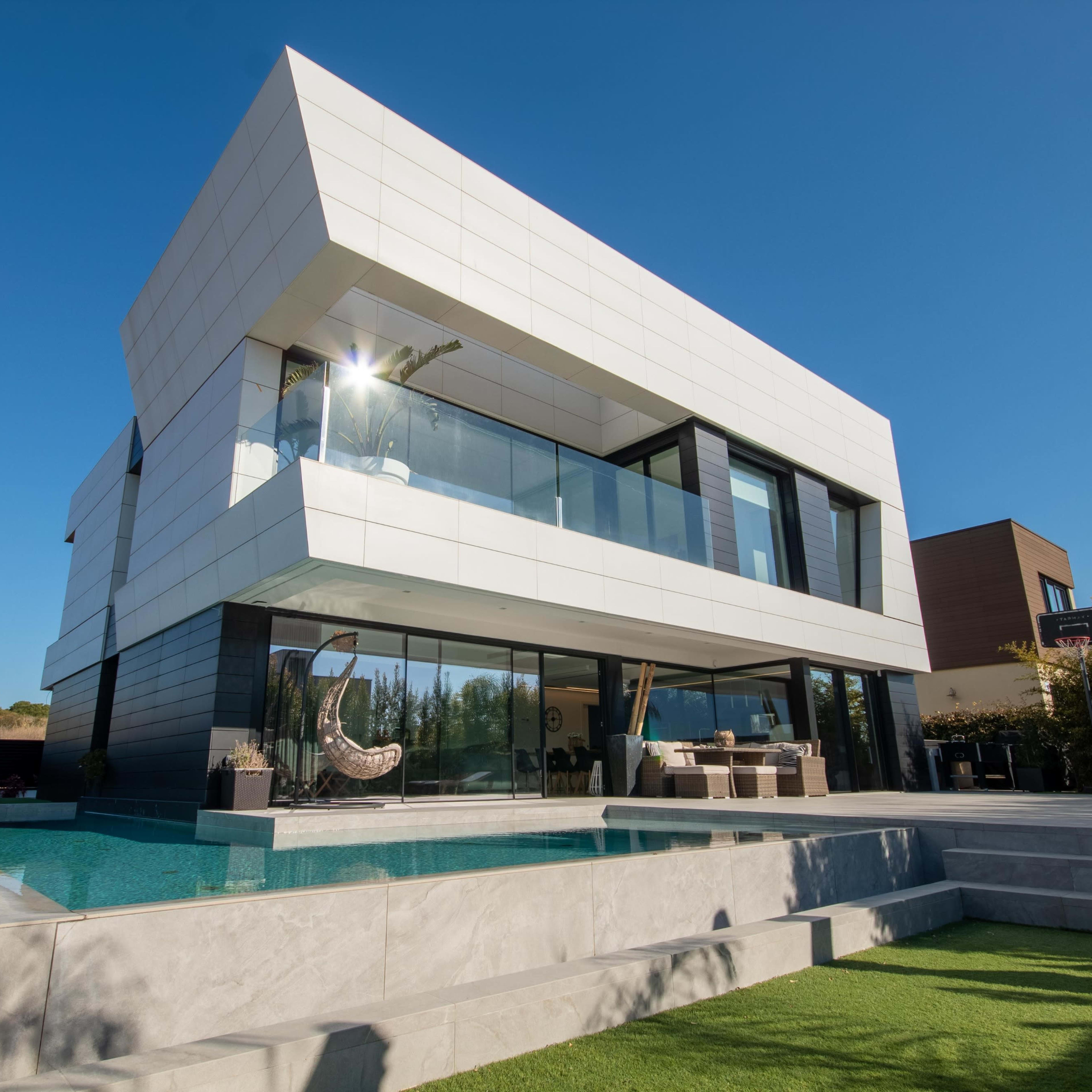 A modern house with a sleek white exterior, large glass windows, and a pool in the backyard.