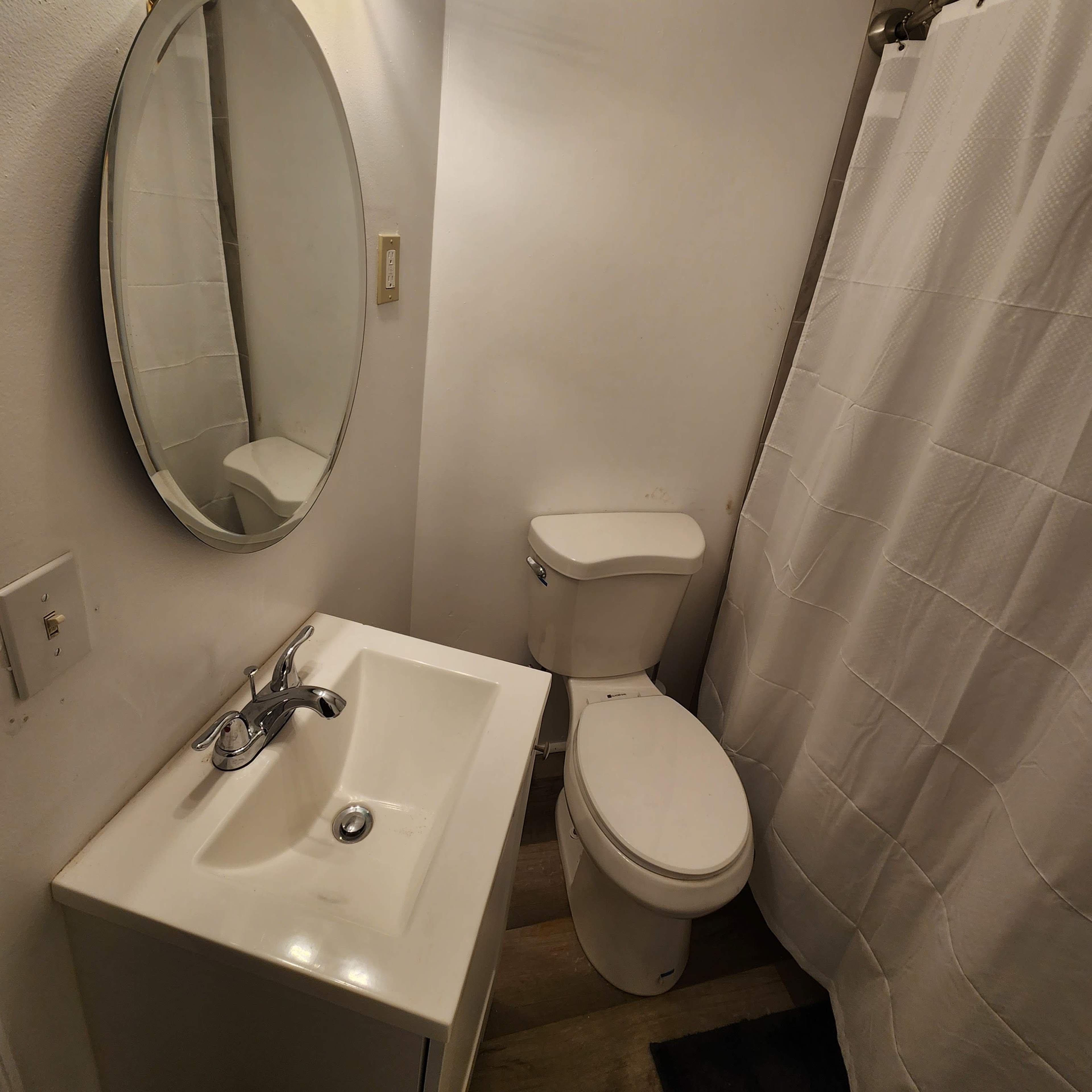 A small bathroom with a round mirror above a white sink and a toilet next to a shower curtain.