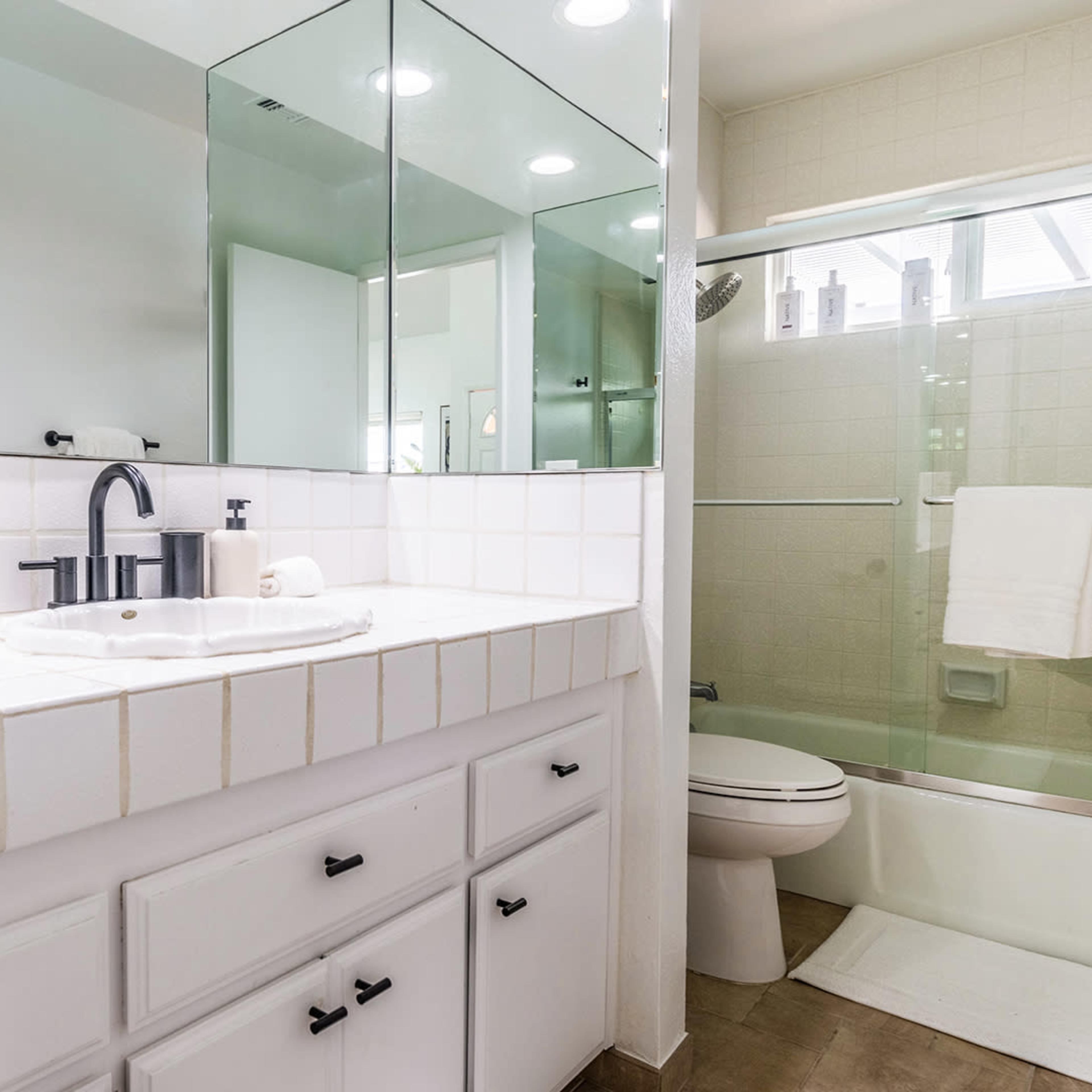 A clean bathroom with a white tiled sink, a mirror above it, and a glass shower enclosure.