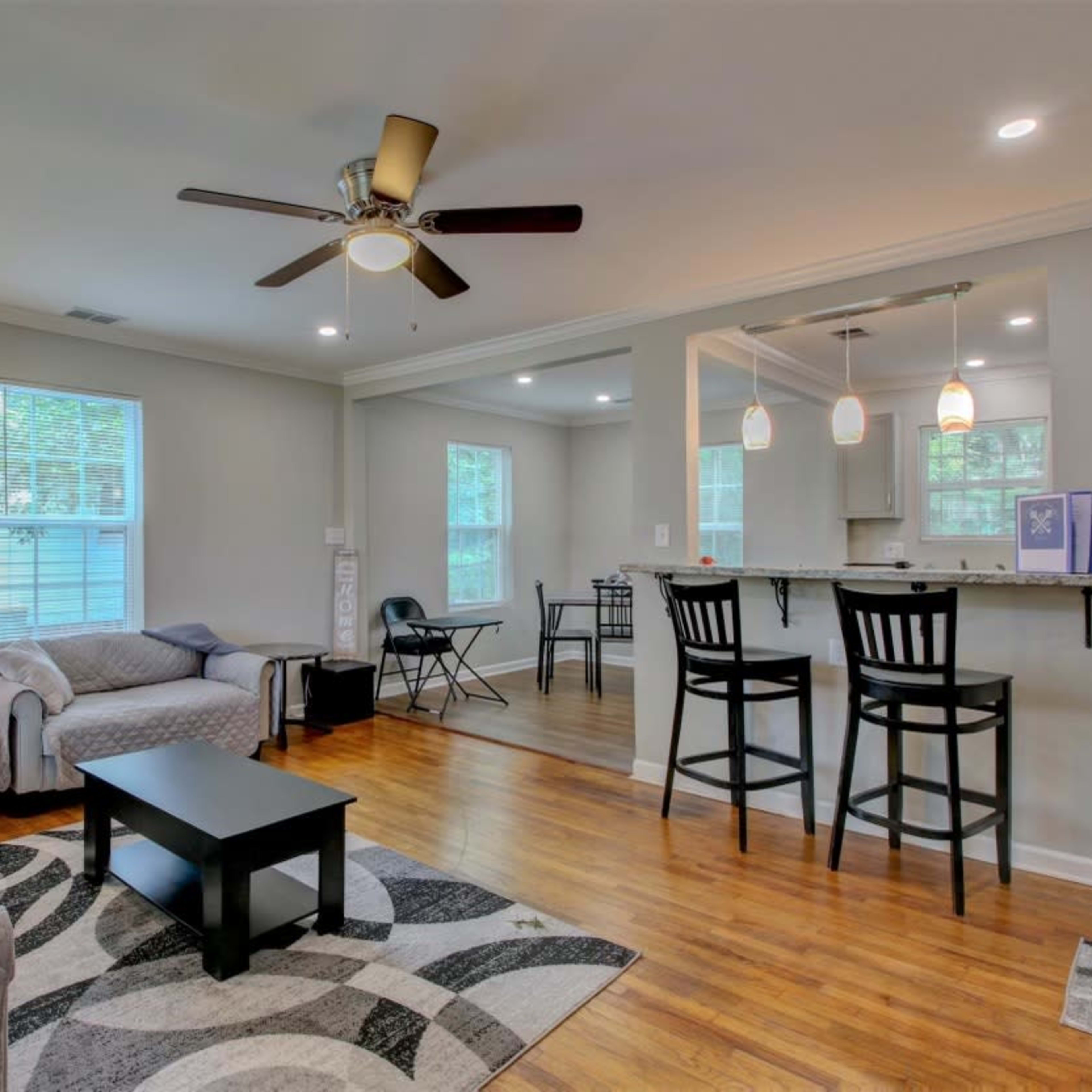 A living area with a sofa and chairs, a coffee table, and a ceiling fan, leading to an adjoining dining area with a table and chairs.