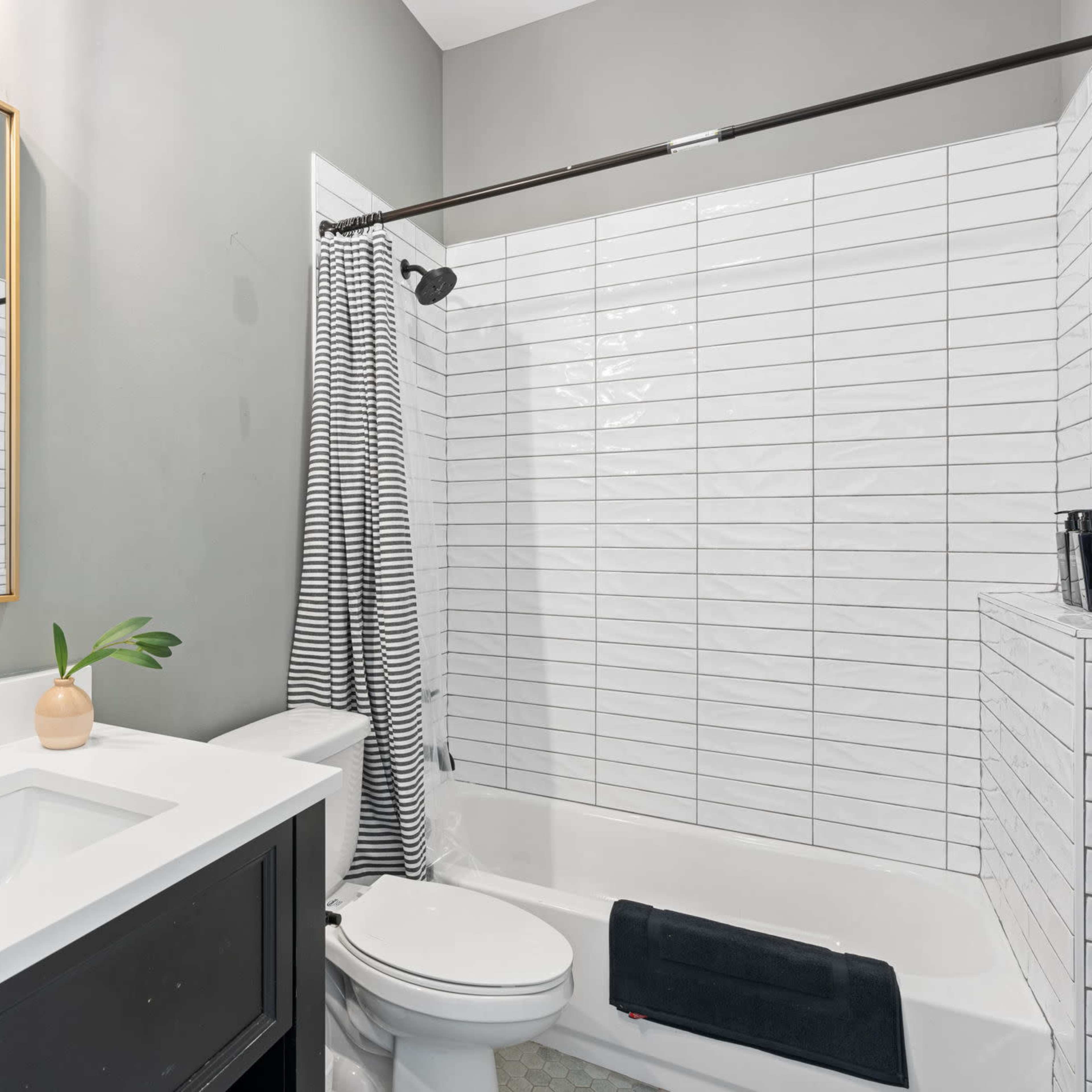 A modern bathroom features a white countertop sink, a bathtub with a shower curtain, and gray walls adorned with a mirror and minimalist decor.