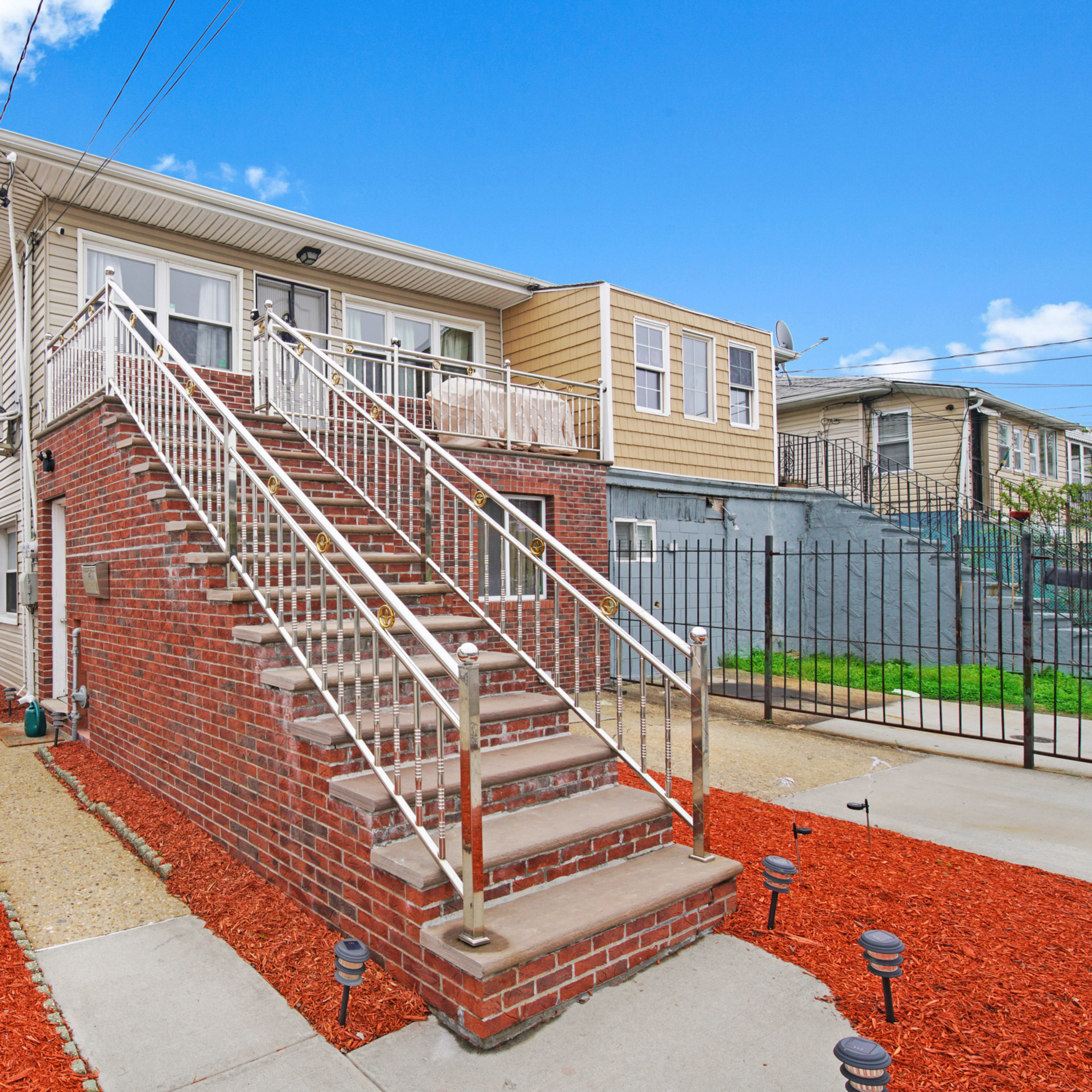 A two-story brick building with a set of stairs leading to the entrance, surrounded by a gravel path and red mulch landscaping.