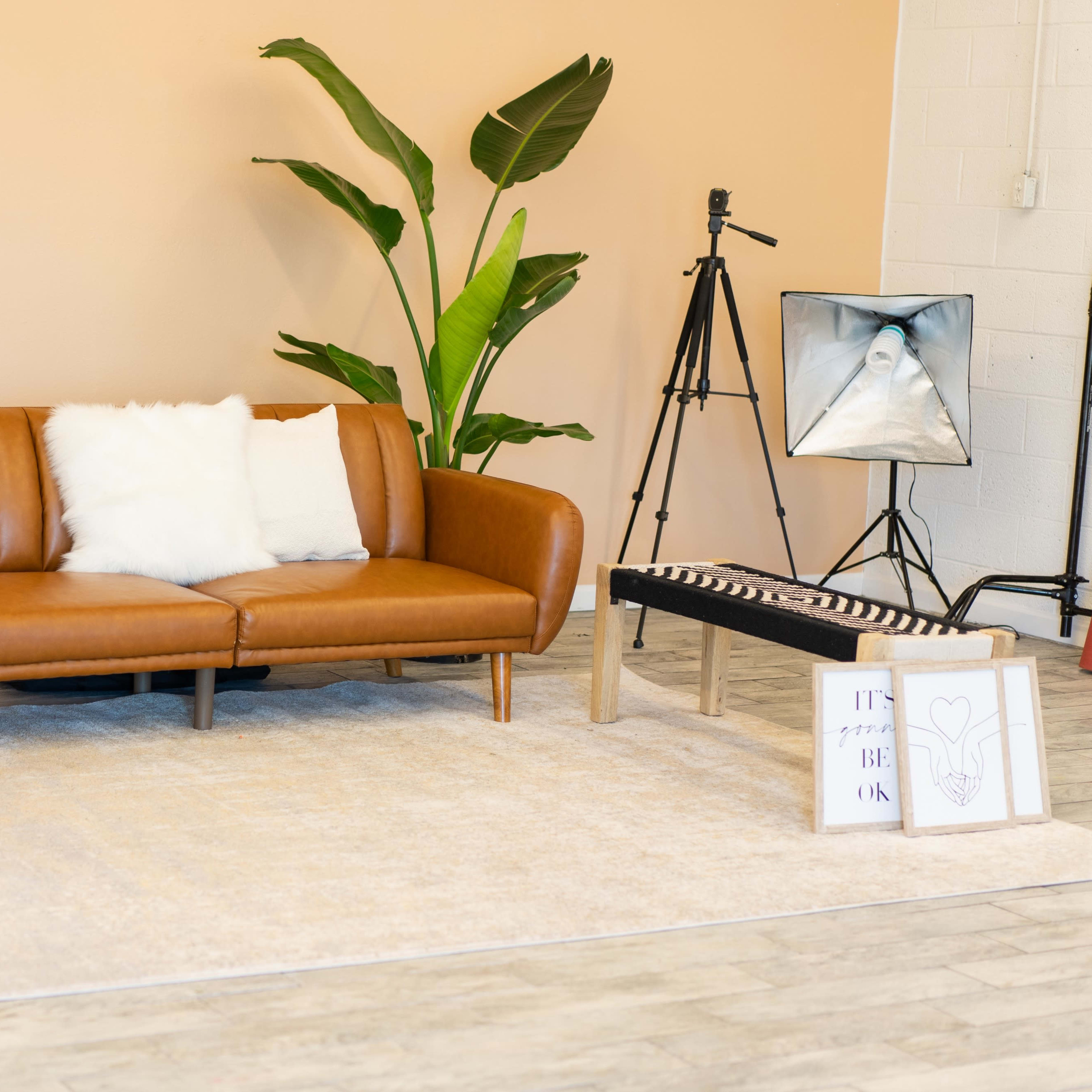 A modern living room setup with a brown leather sofa, two green-accented side tables, a large mirror, a plant, and a small coffee table with decorative items.