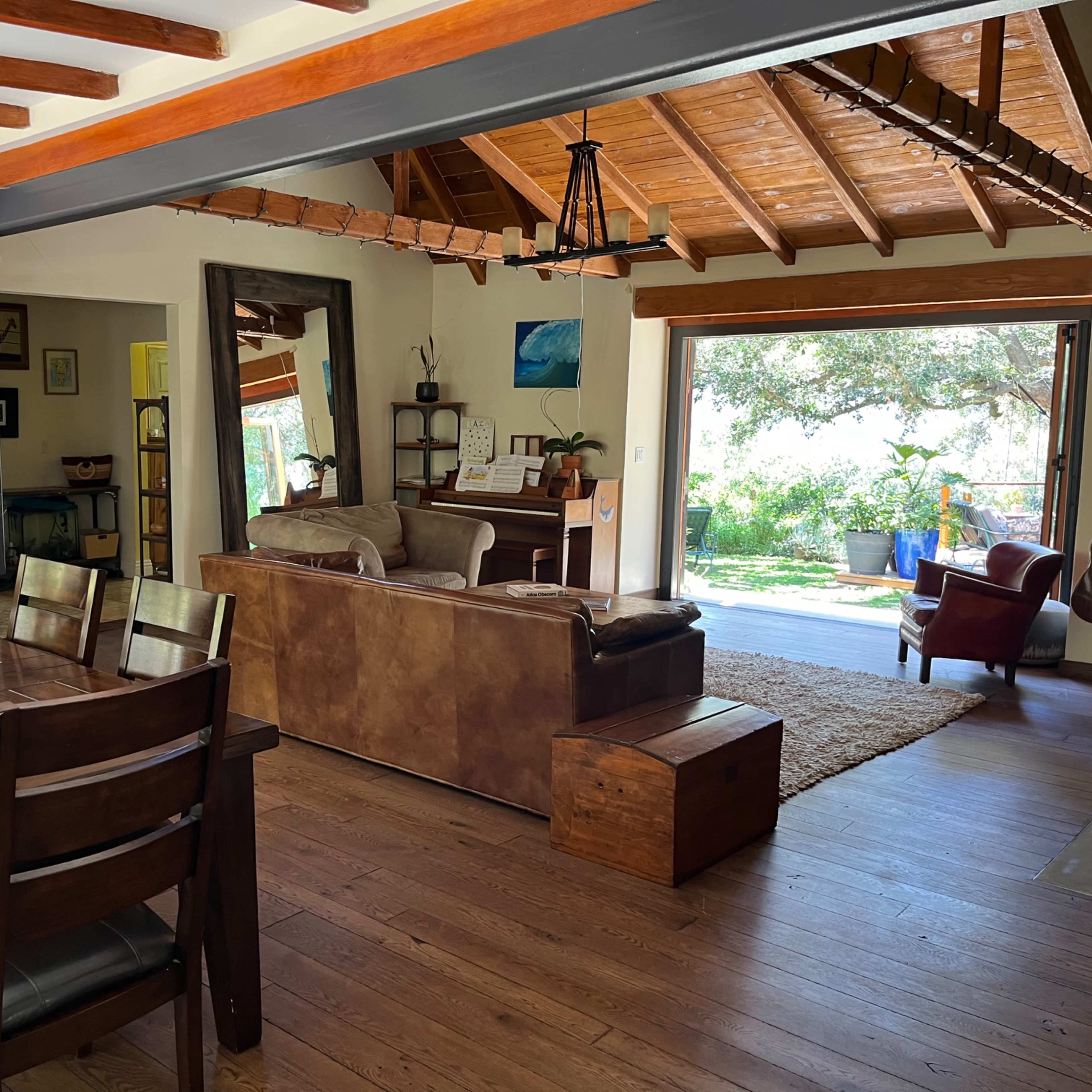 A spacious living area features a dining table, a leather sofa, and an open doorway leading to a garden.