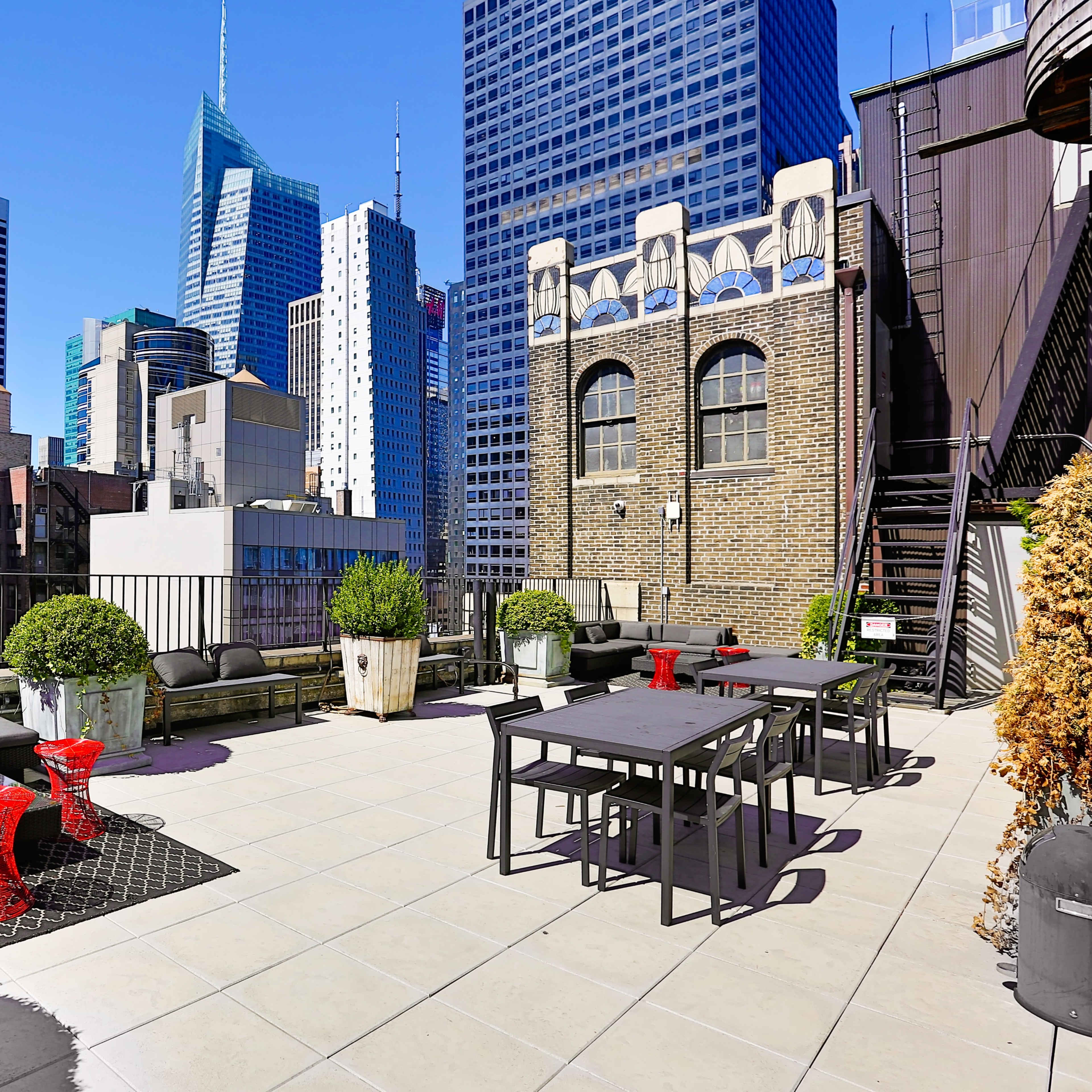 The rooftop terrace features modern seating and dining areas with views of skyscrapers in a bustling city skyline.