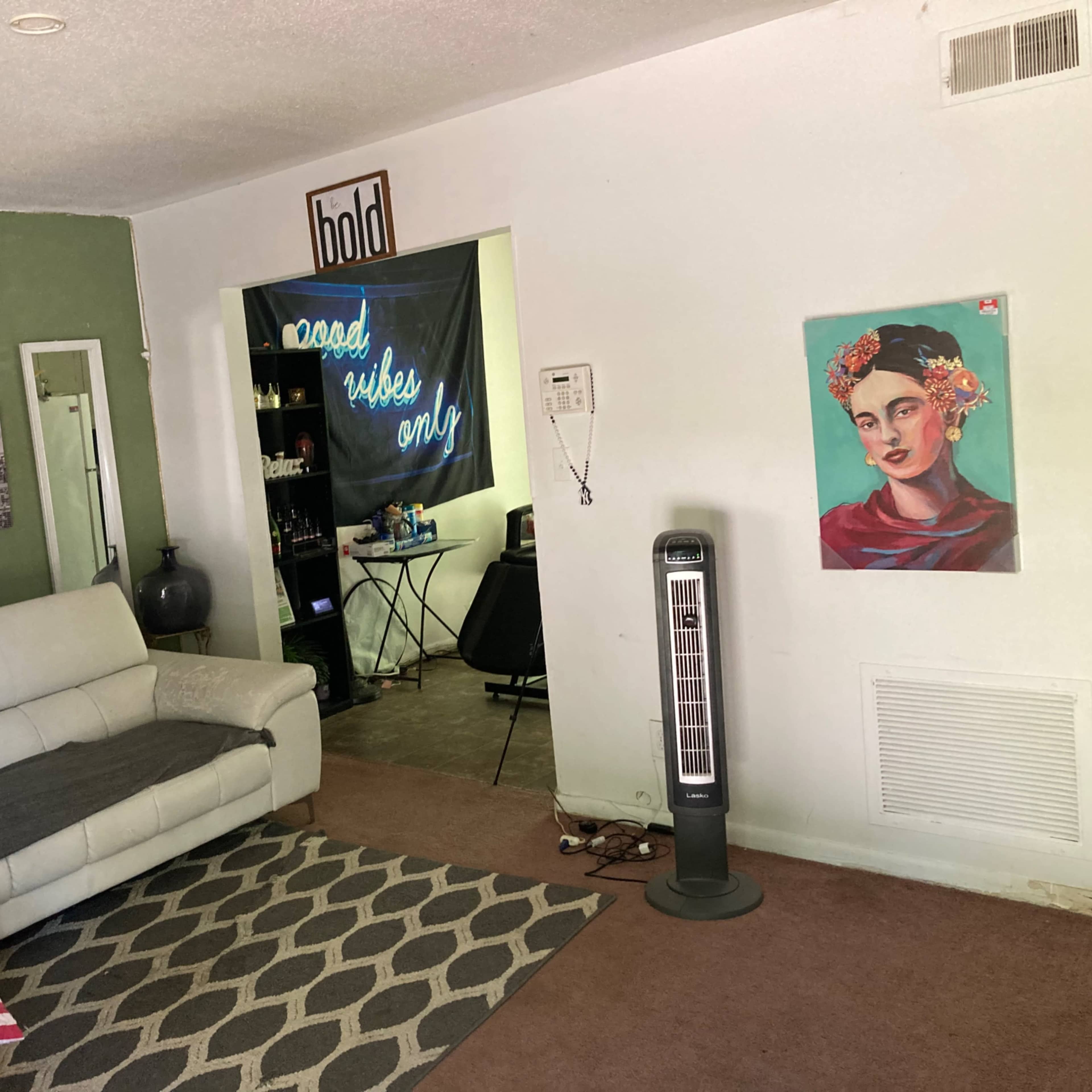 A living room with a white sectional couch, a rug with a geometric pattern, and a wall adorned with a portrait of a woman and various framed prints.