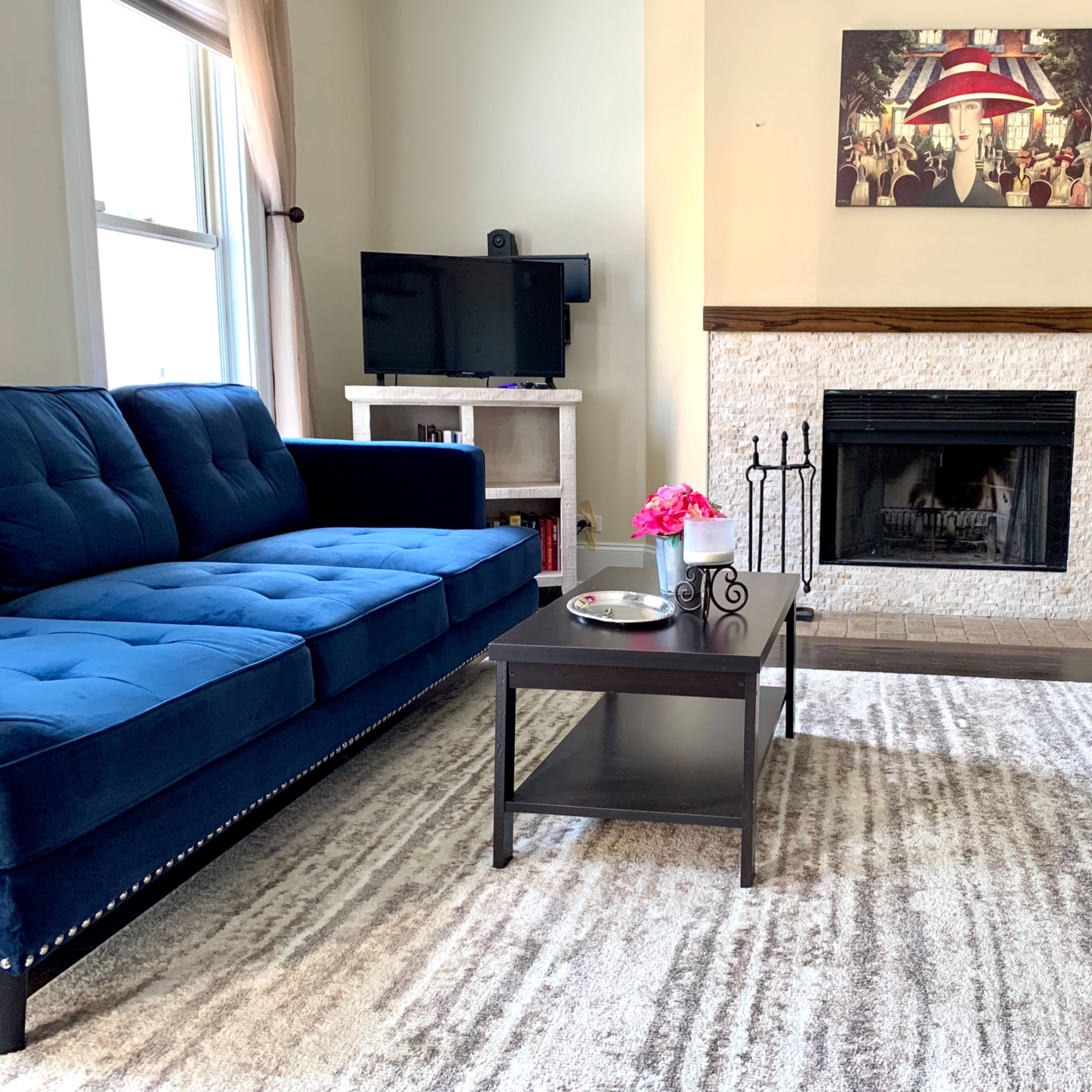 A modern living room with two blue sofas, a coffee table with a small vase of flowers, and a fireplace surrounded by light-colored stone.