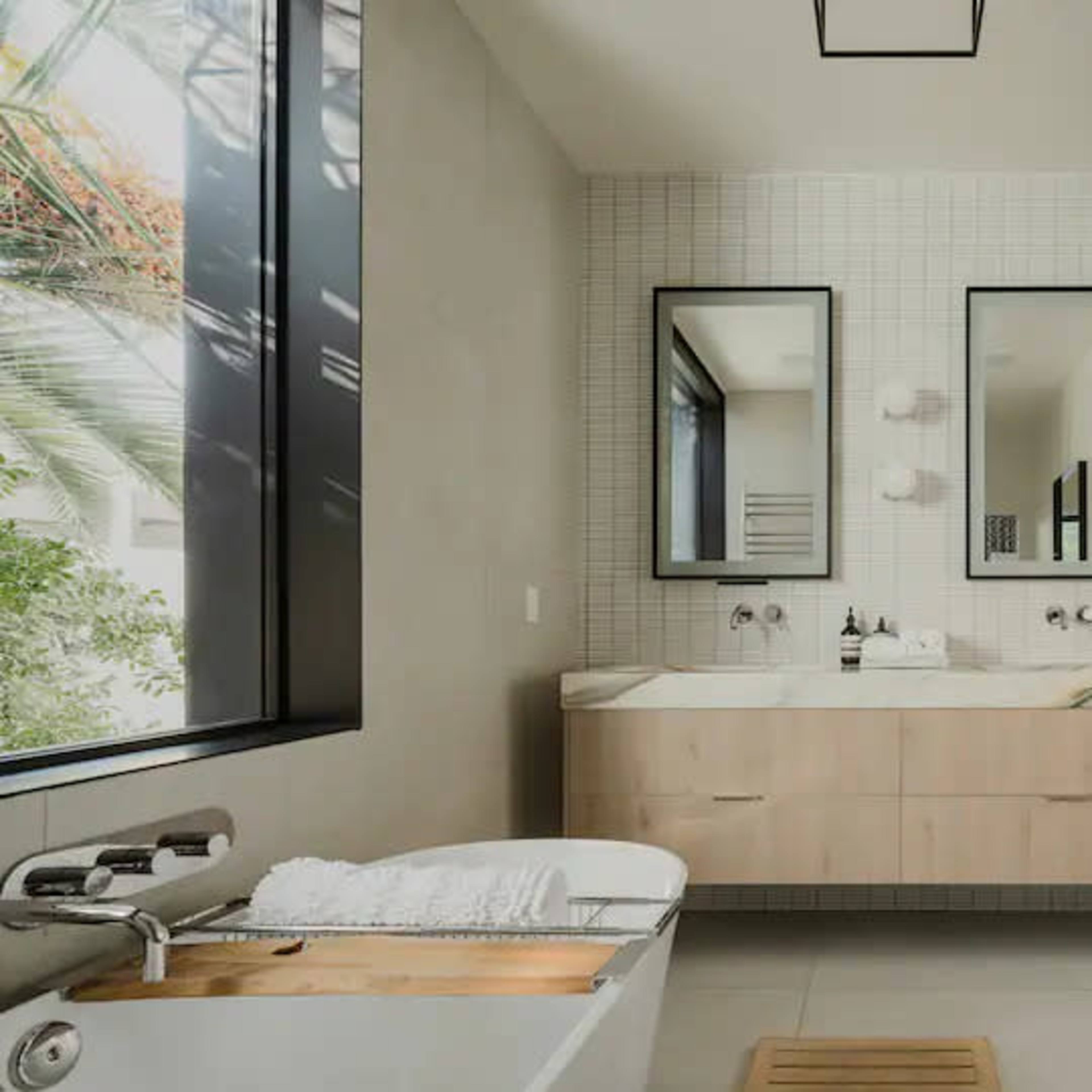 A modern bathroom featuring a freestanding bathtub, double sinks with mirrors, and a wood vanity against a tiled wall.