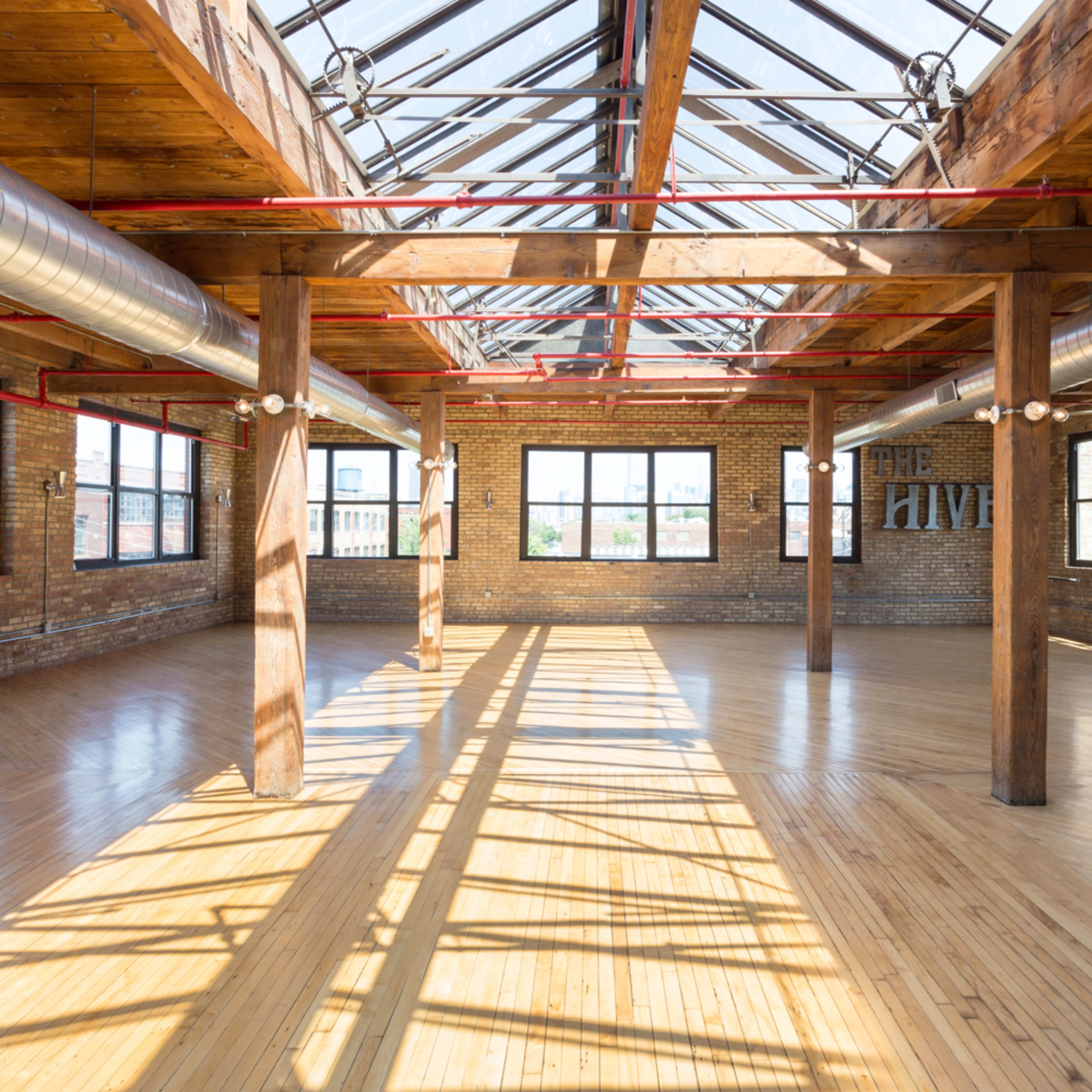 A spacious, well-lit loft with wood beams, large windows, and polished wooden floors.
