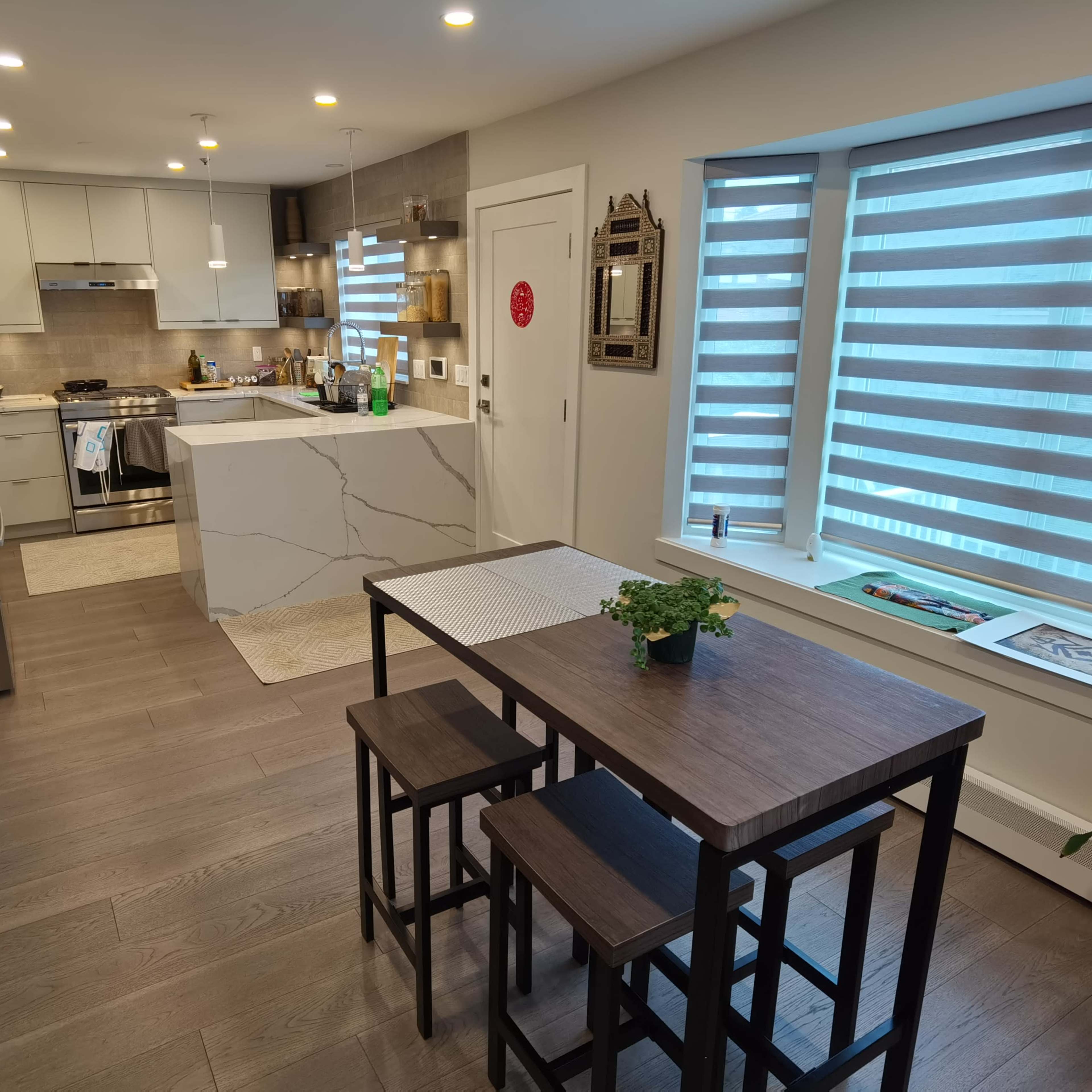 A modern kitchen and dining area with a small table and two chairs, featuring sleek cabinets and a large island counter.
