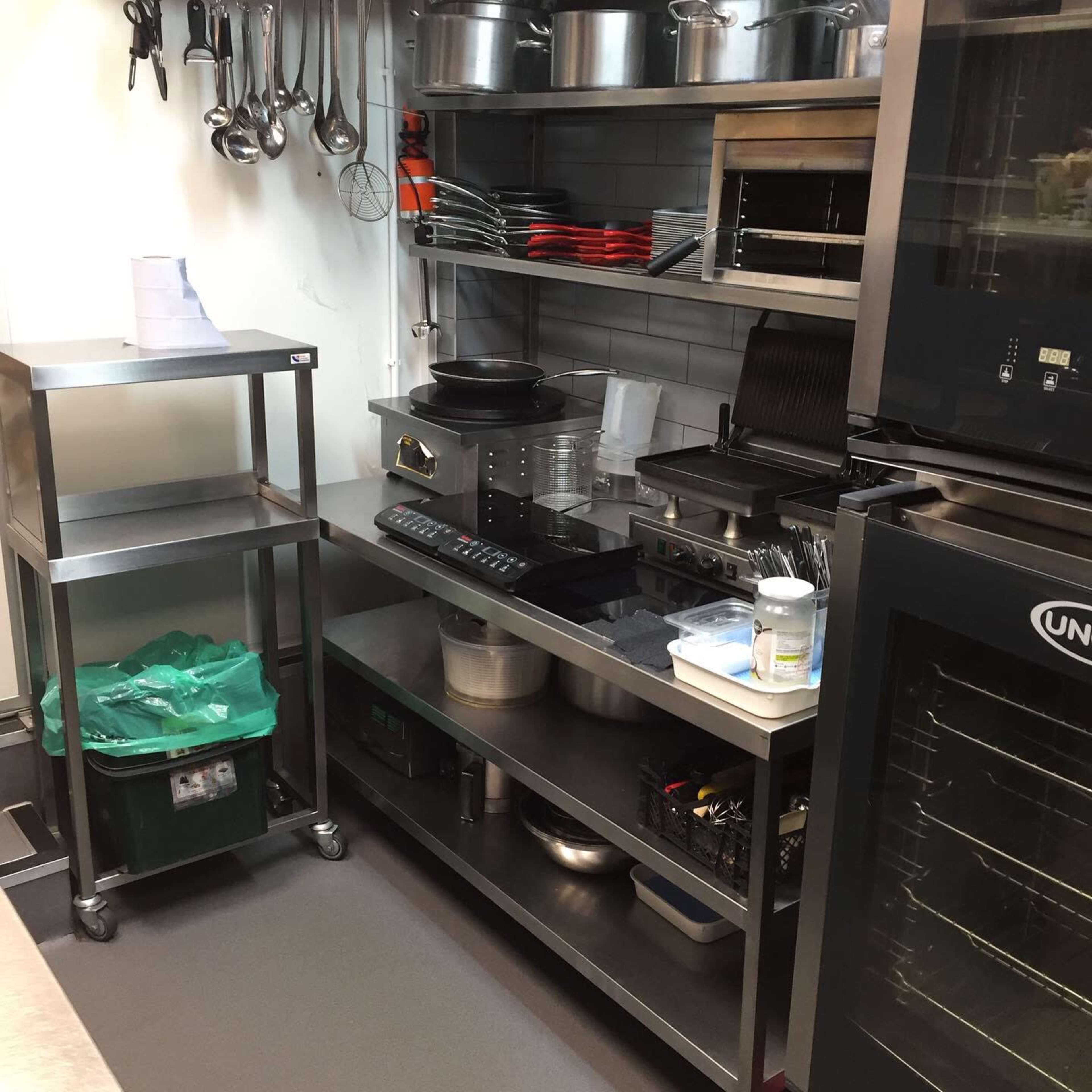 A commercial kitchen with stainless steel counters, cooking equipment, and various utensils organized on shelves.