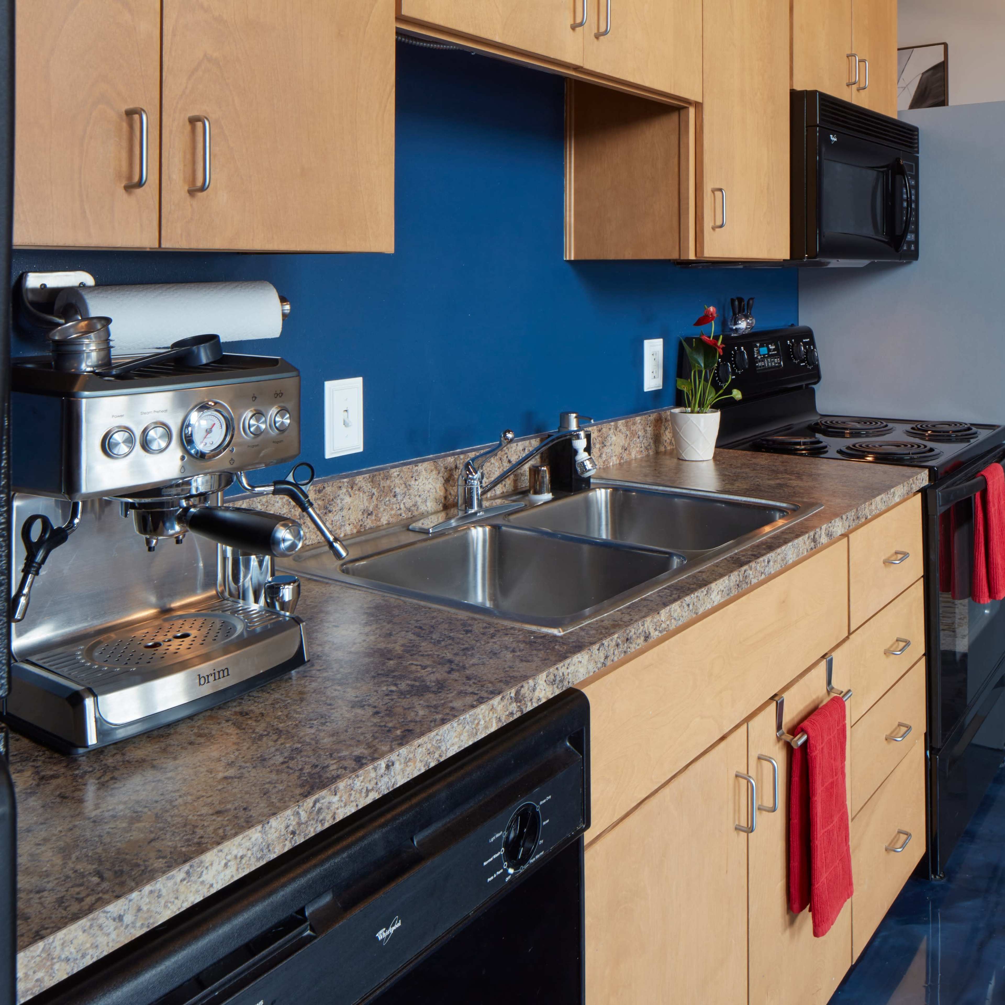 A modern kitchen with wooden cabinetry, a double sink, and kitchen appliances including a coffee machine and a black refrigerator.