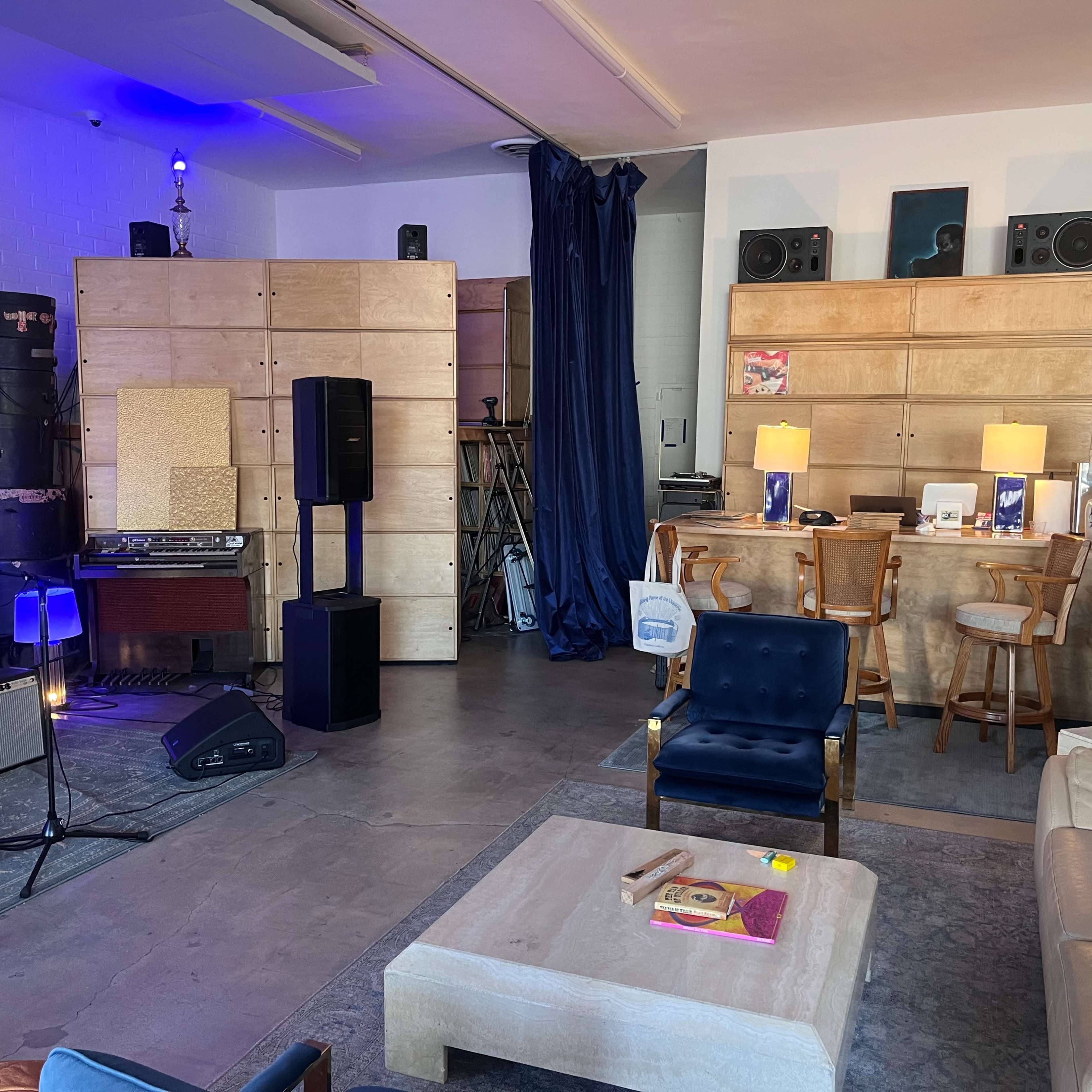 A cozy music studio or lounge area featuring various audio equipment, seating, and wooden shelving units.