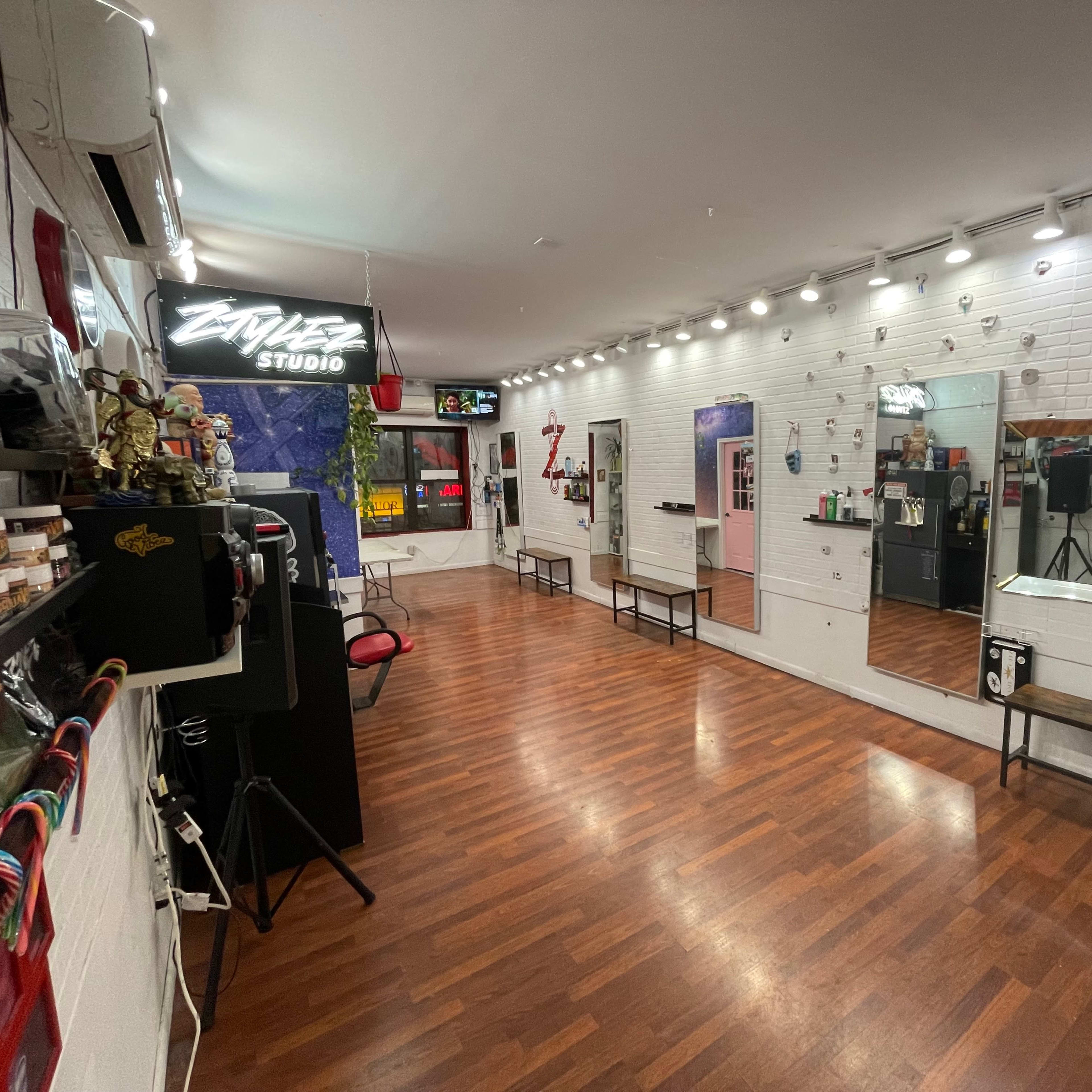 A well-lit hair studio with wooden flooring, mirrors, and various styling equipment arranged neatly along the walls.