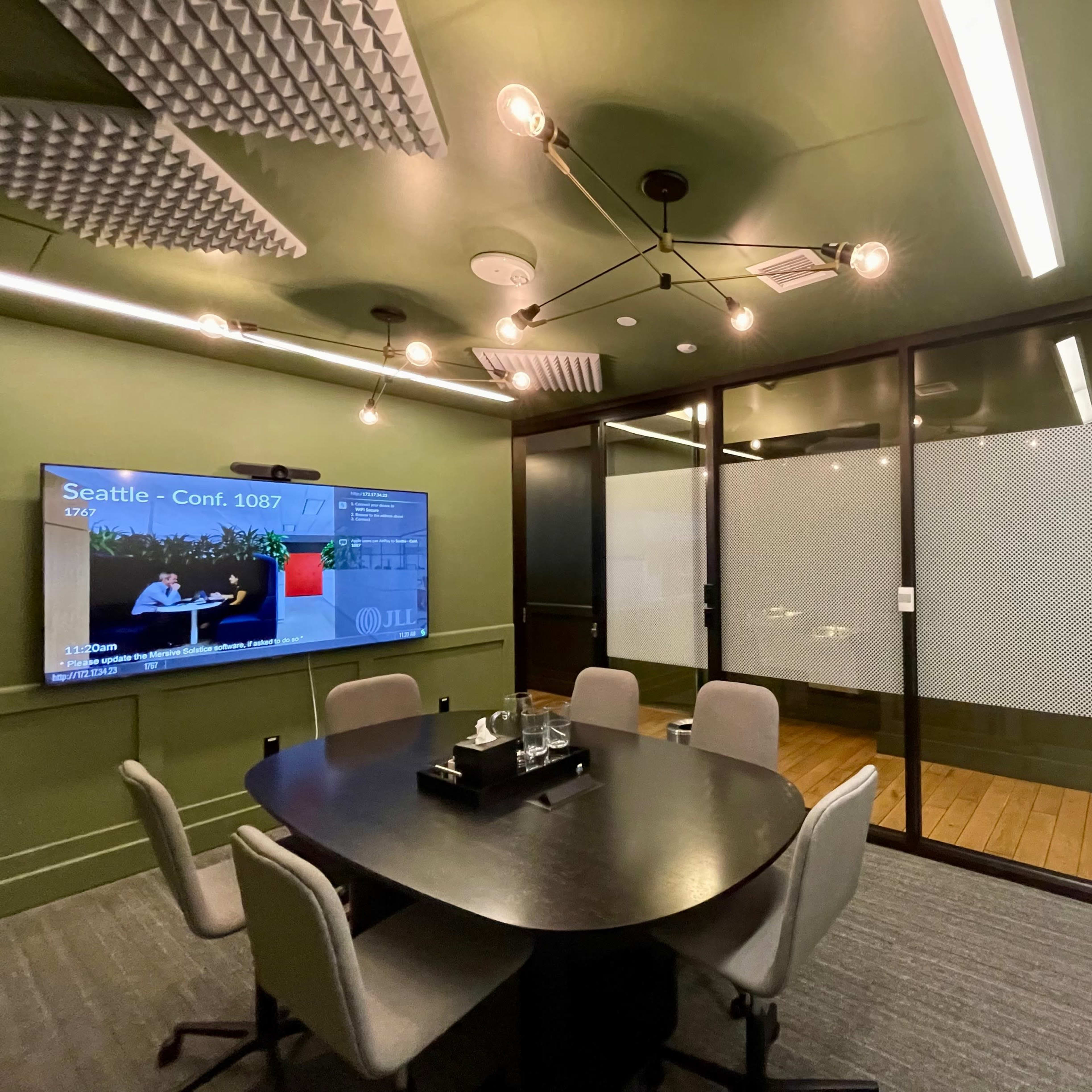 A modern conference room with a round table, ergonomic chairs, a large display screen, and a glass-walled meeting area.