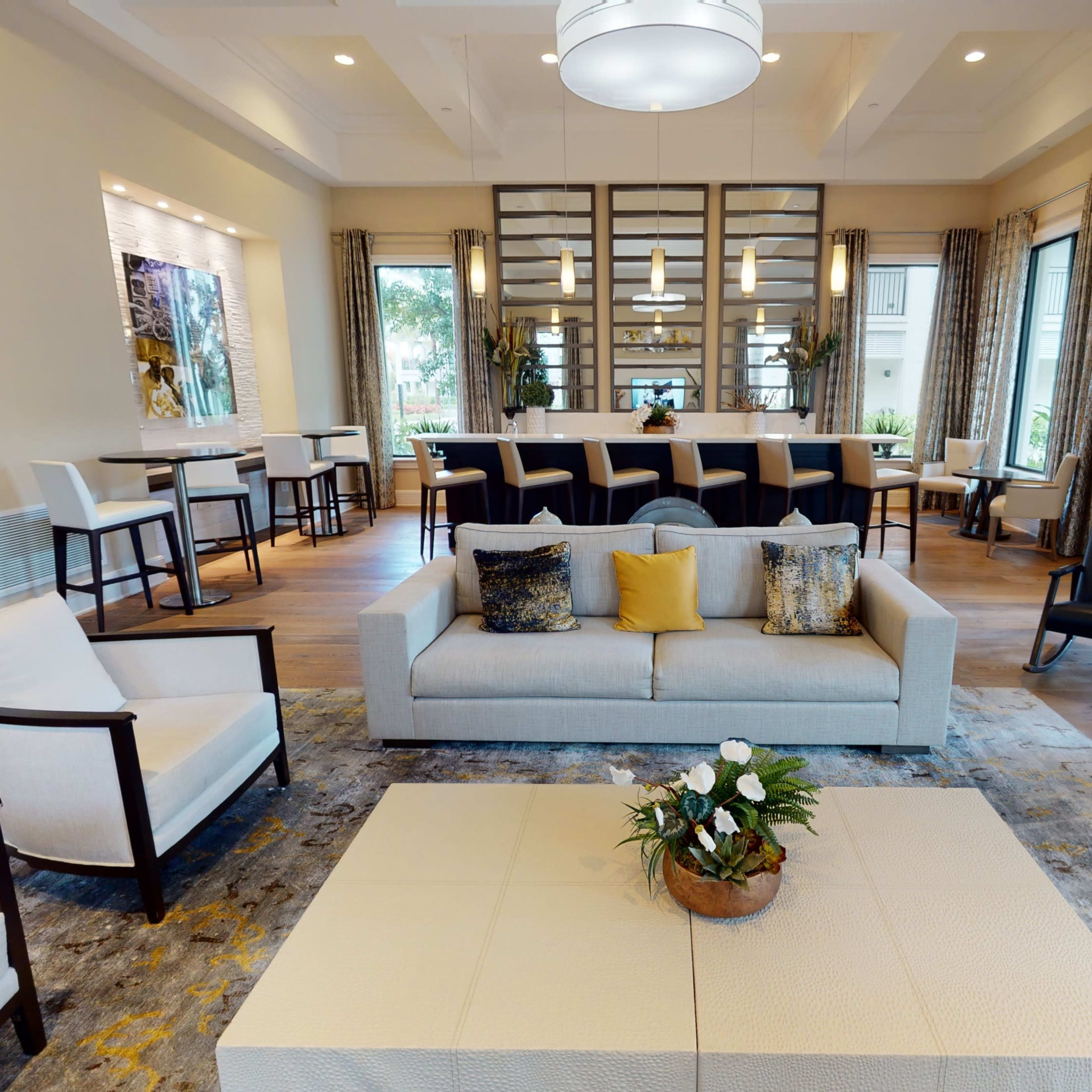 A modern lounge area with a light-colored sofa, several seating options, a coffee table, and large windows allowing natural light.