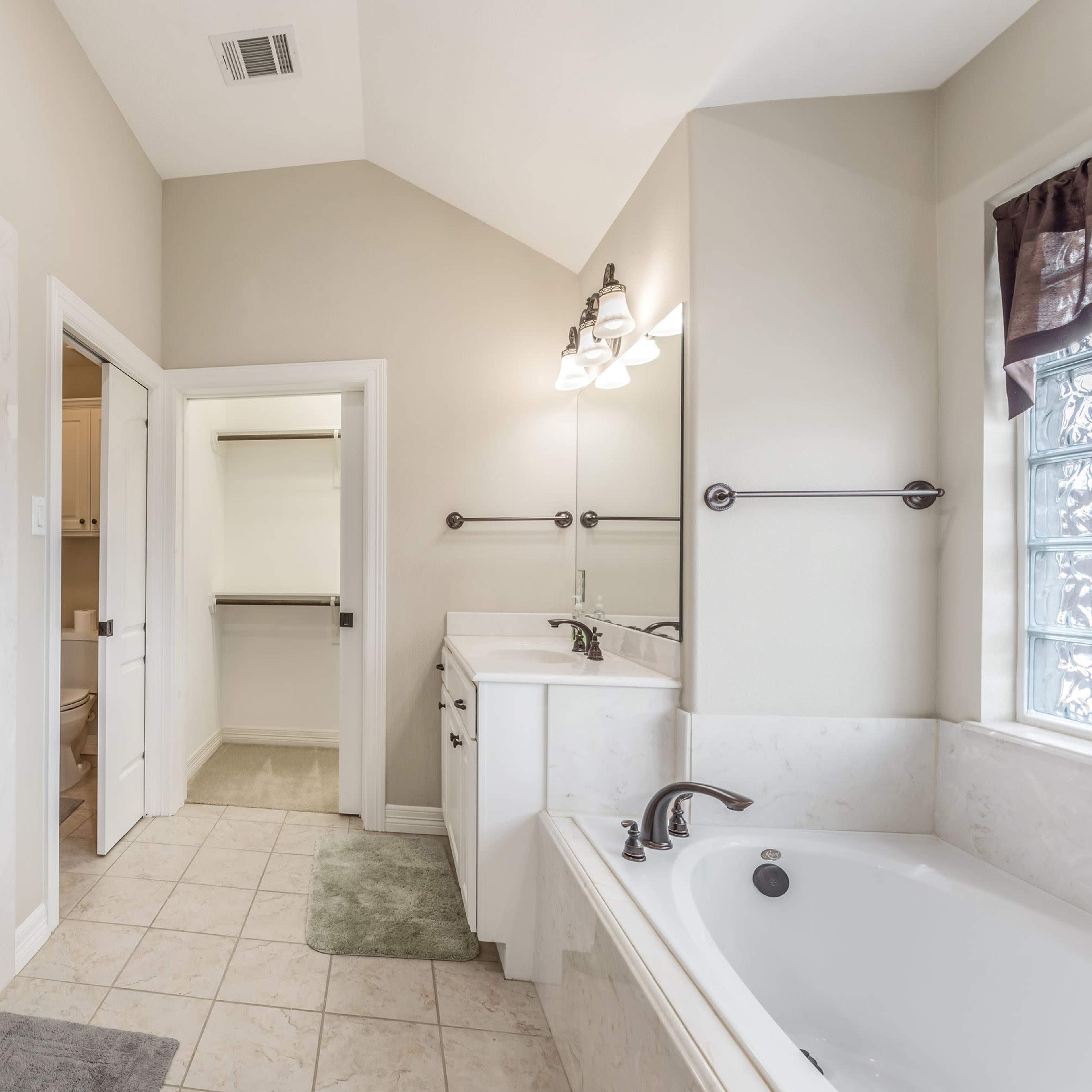 A well-lit bathroom featuring a shower area, a bathtub, and a double vanity with mirrors.
