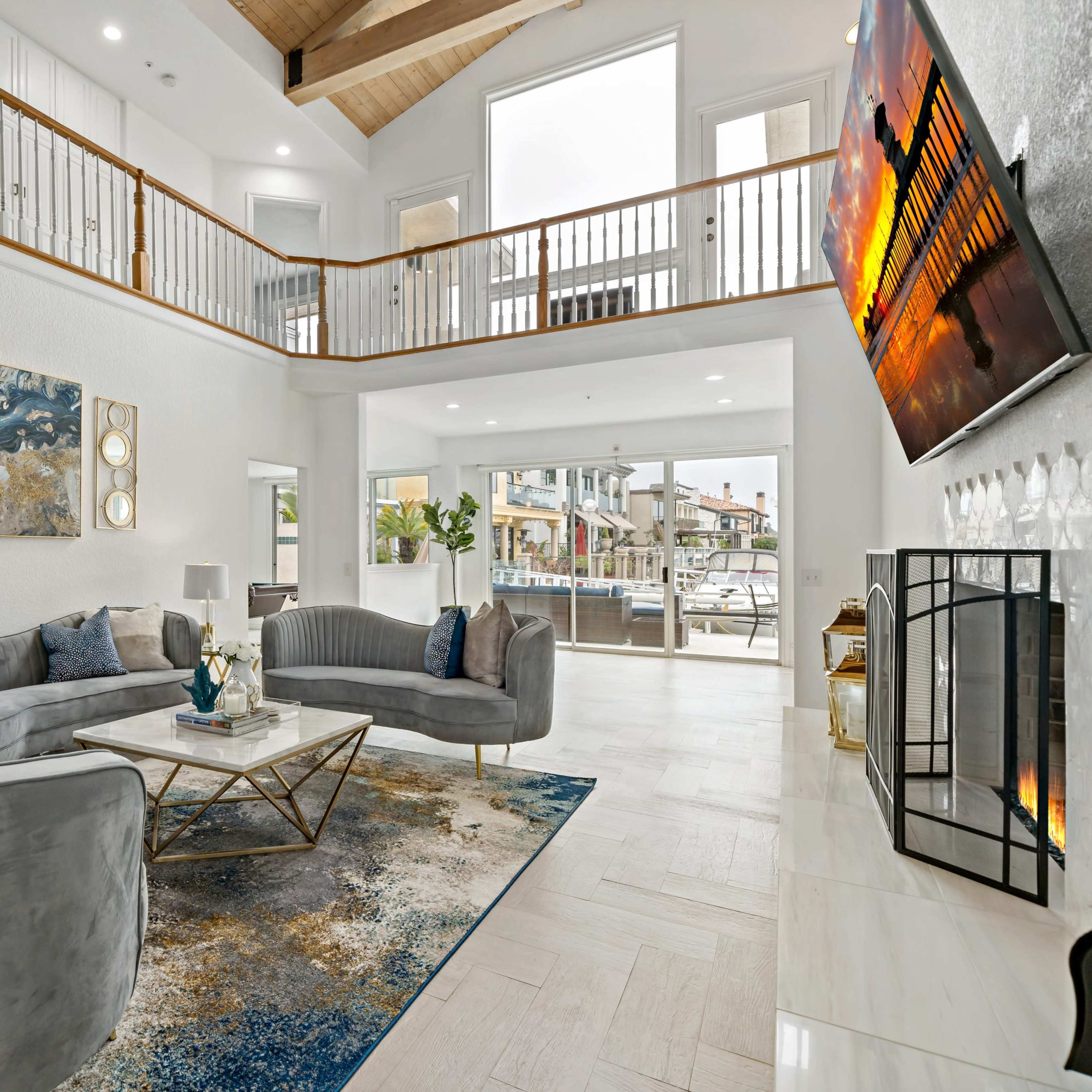 A spacious living room features two gray sofas facing a coffee table, with large windows and a view of an outdoor area.