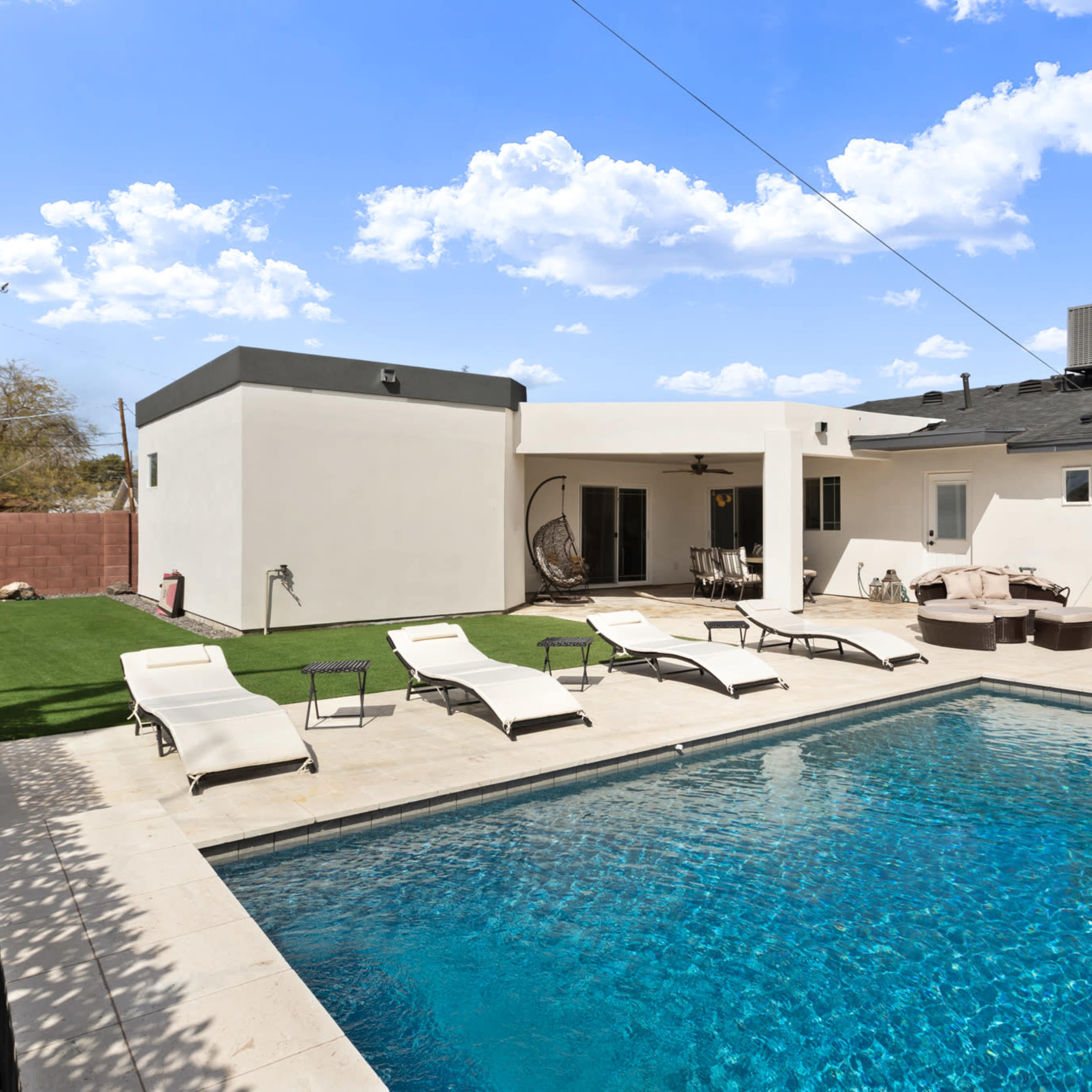 A backyard with a swimming pool surrounded by lounge chairs and a patio area with seating.