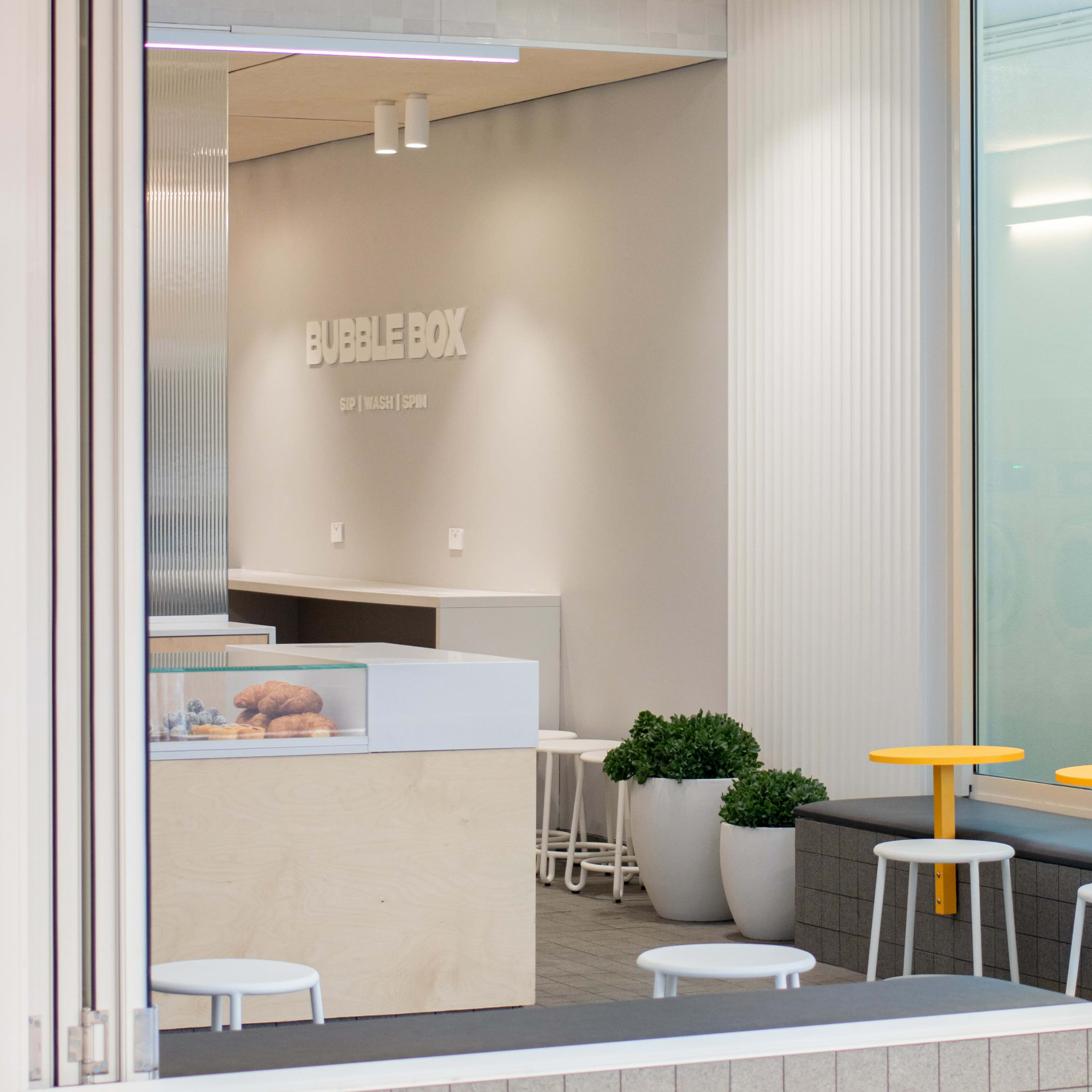 A modern café interior with a minimalist design, featuring light-colored walls, simple furniture, and a sign that reads "BUBBLE BOX."