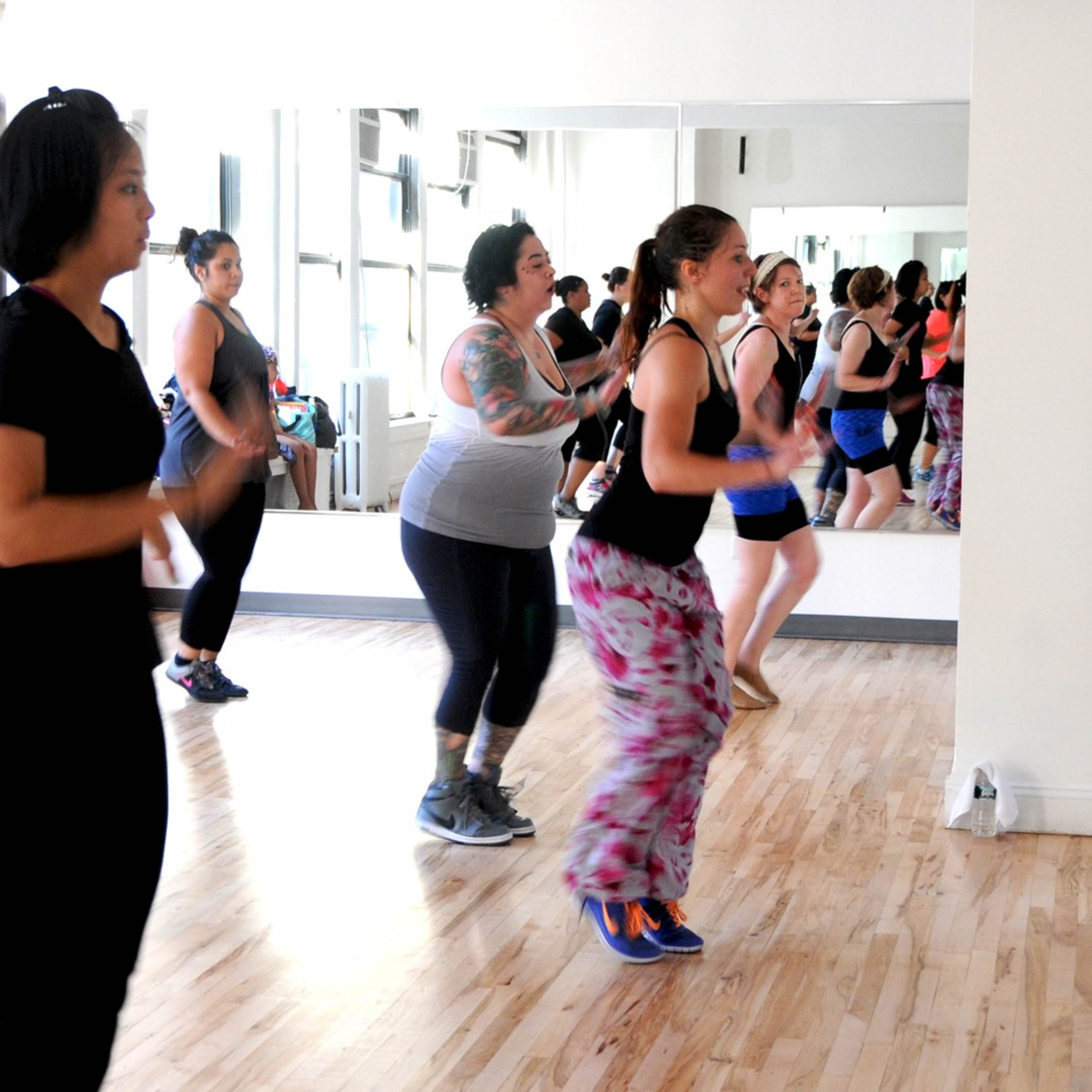 A group of women are participating in a dance class in a studio with mirrors and wooden floors.
