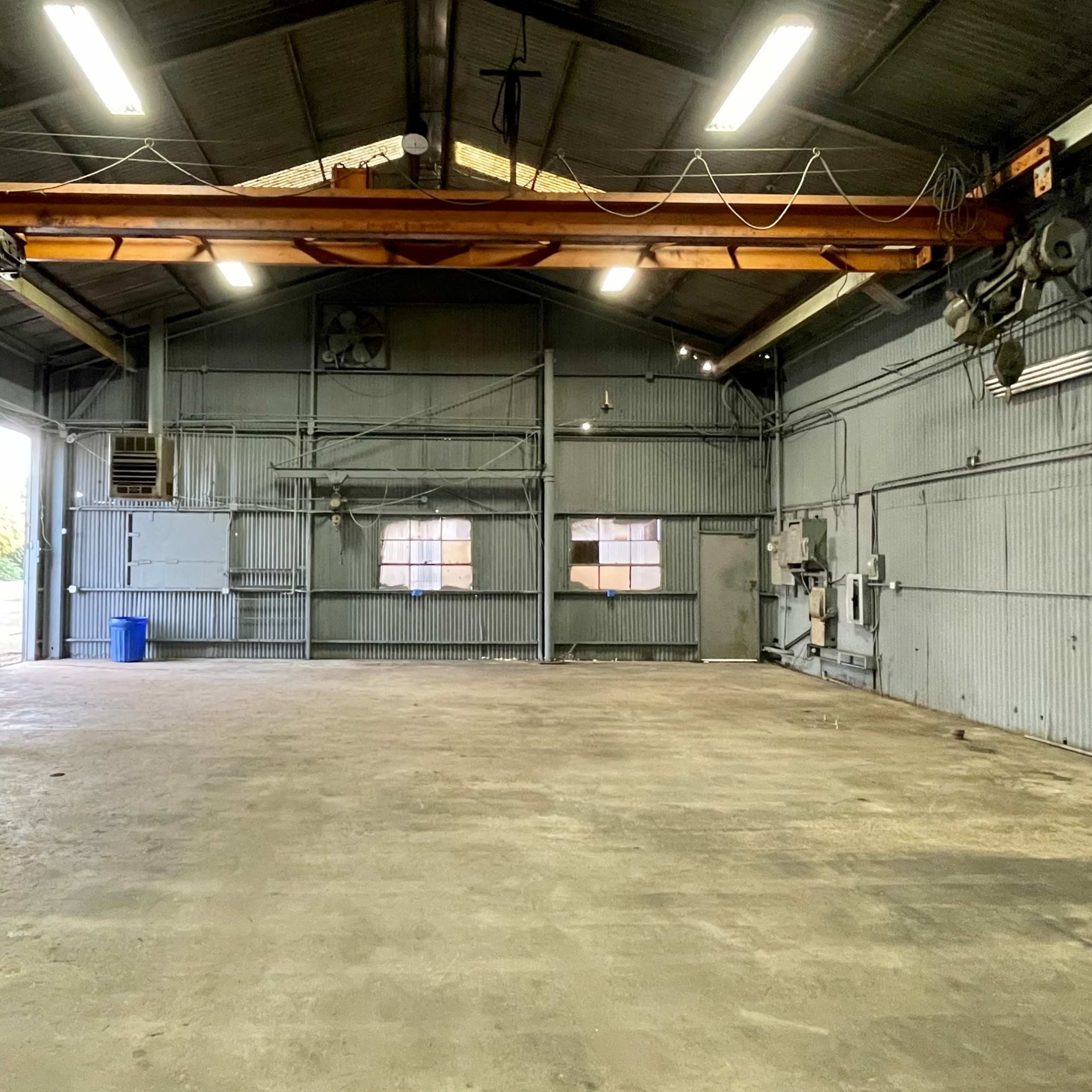 An empty industrial warehouse with a high ceiling, overhead crane, and concrete floor.
