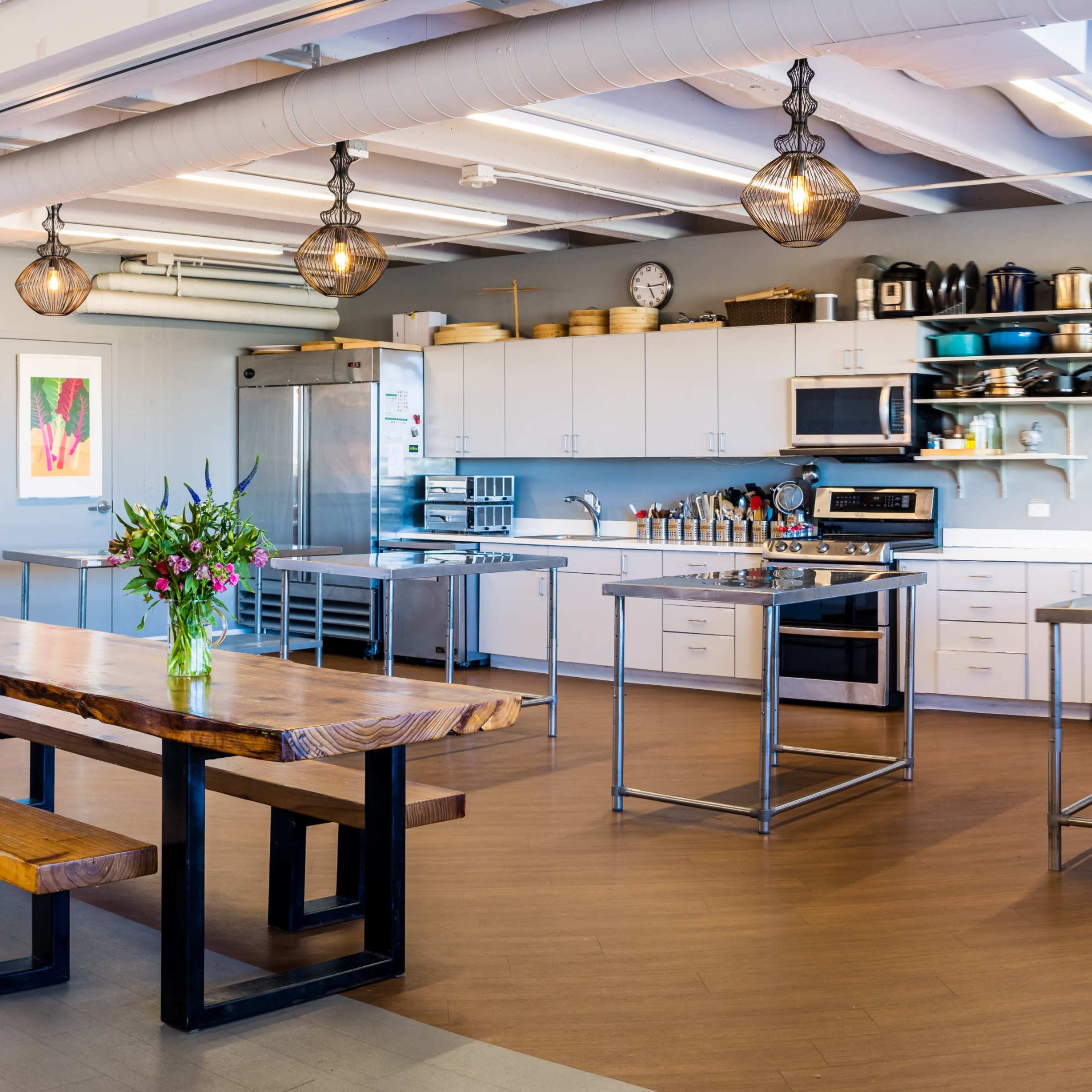 A modern kitchen space featuring a large wooden table, stainless steel appliances, and various kitchenware neatly arranged on shelves.